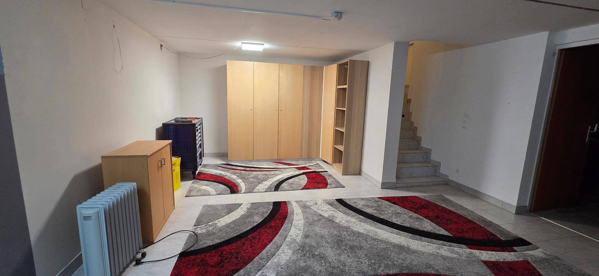 Geräumiger Kellerraum mit Teppichen, Schränken und Treppenzugang, vielseitig nutzbar.