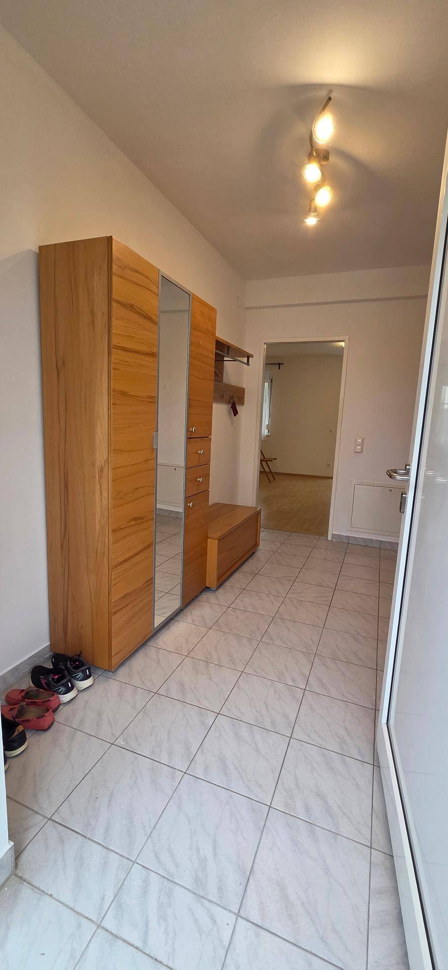 Heller Eingangsbereich mit Fliesenboden und Holzgarderobe, die zu weiteren Räumen führt.