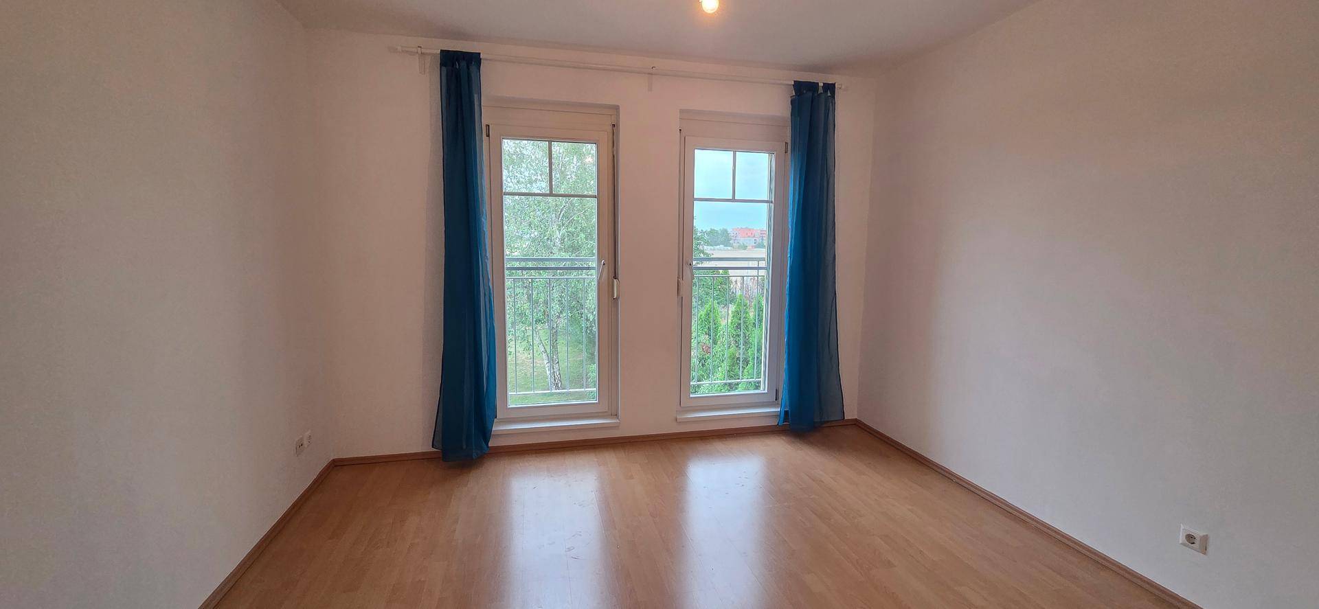 Schlafzimmer mit Laminatboden und zwei Fenstern, die viel Tageslicht hereinlassen.