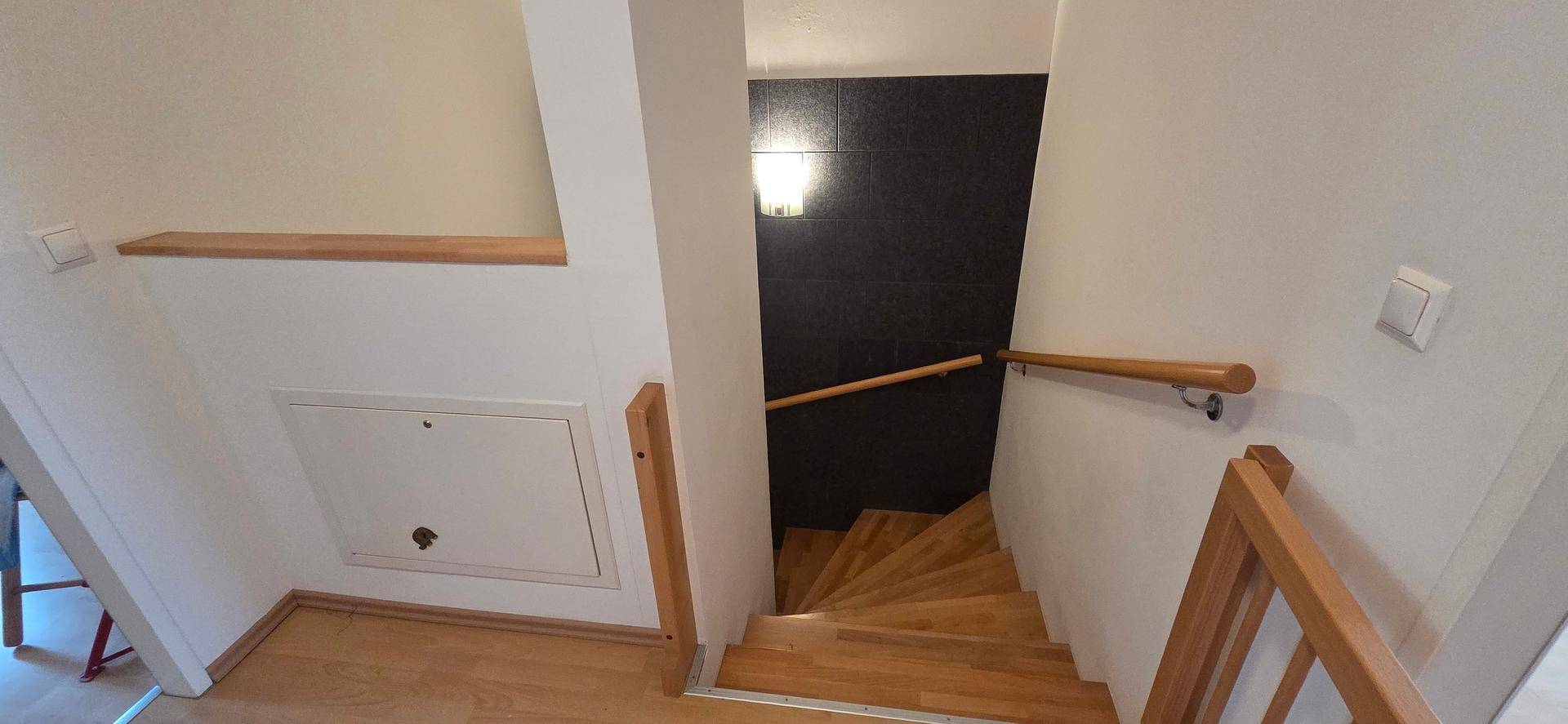 Holztreppe mit Handlauf und dunkler Akzentwand, die die oberen Etagen verbindet.