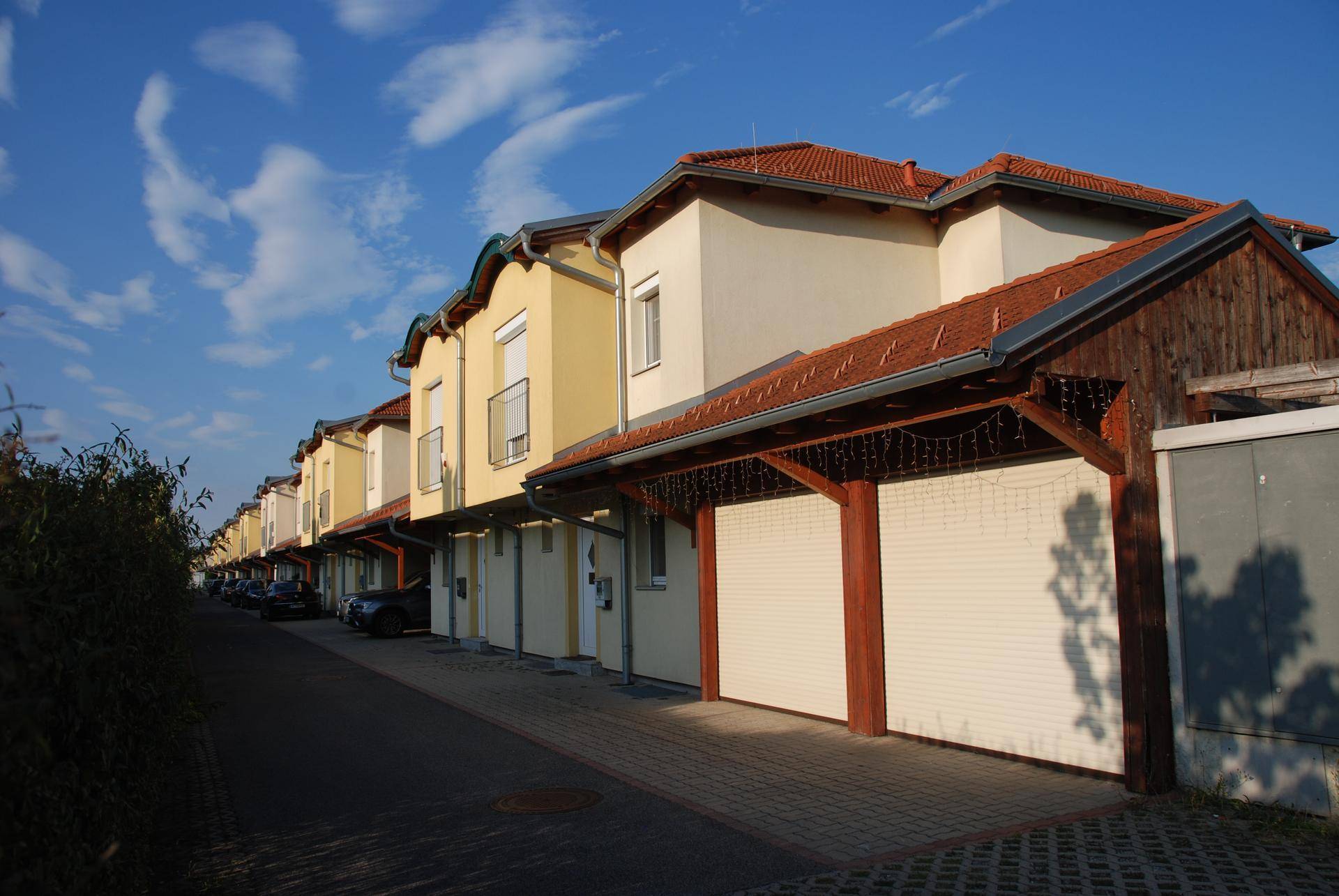 Reihe von Reihenhäusern mit Carports und gepflasterter Zufahrt unter blauem Himmel.