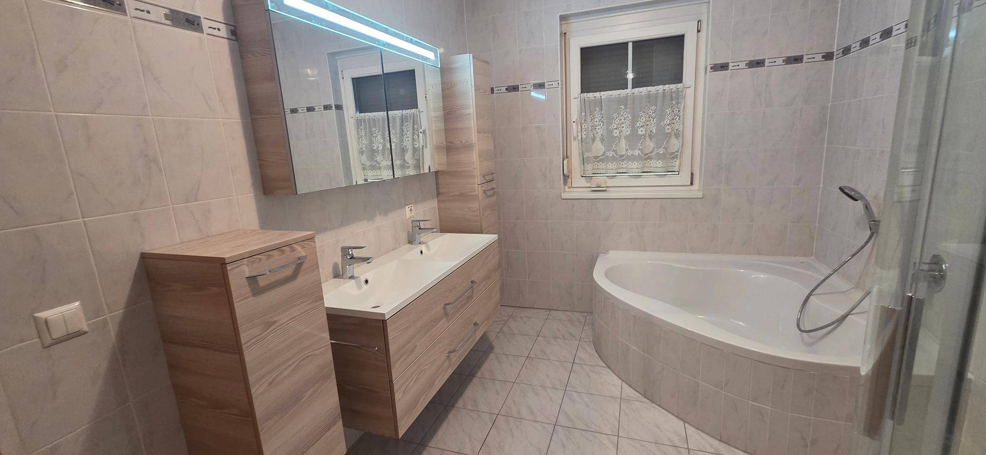 Geräumiges Badezimmer mit Badewanne, Duschkabine, Doppelwaschbecken und Fenster.