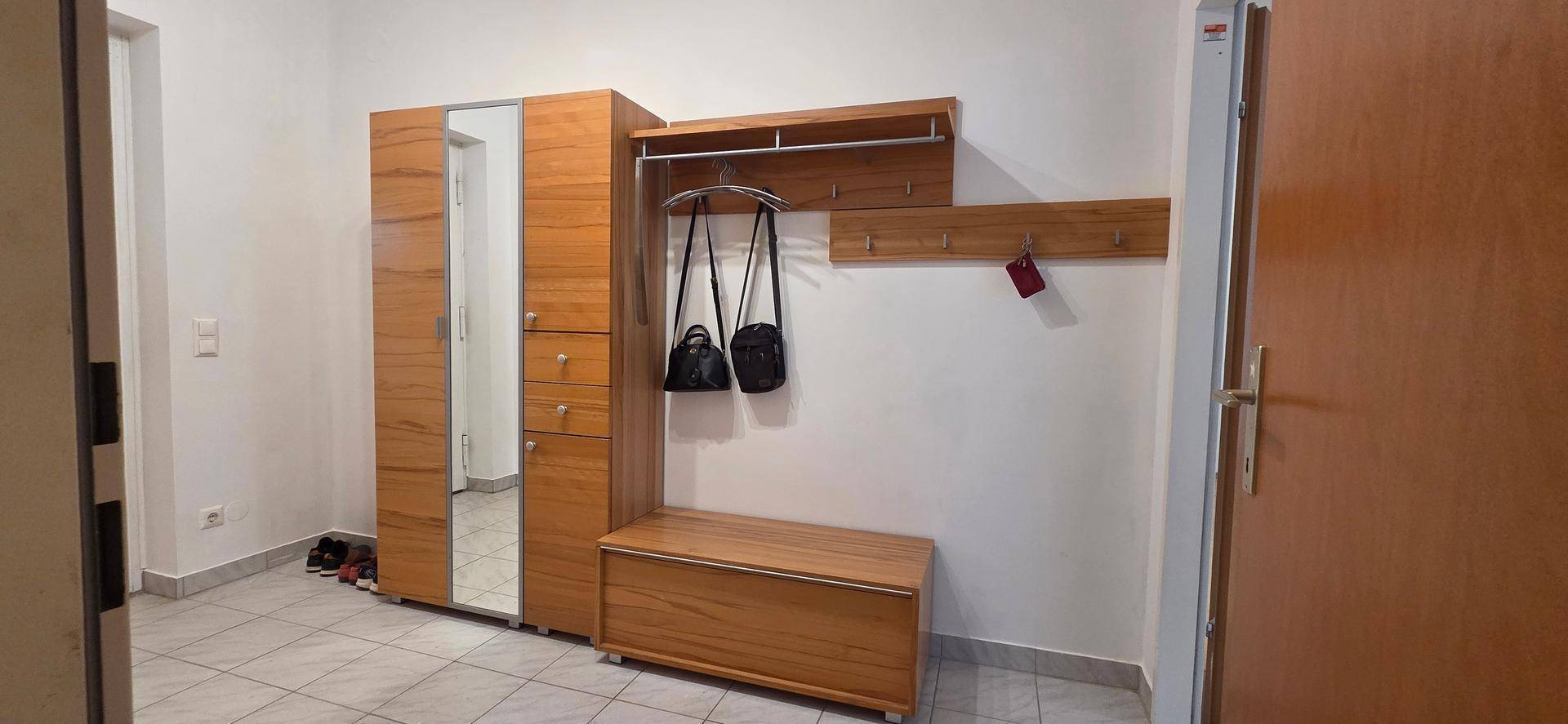 Eingangsbereich mit heller Holzgarderobe, Spiegel und Fliesenboden, ideal für den Empfang.
