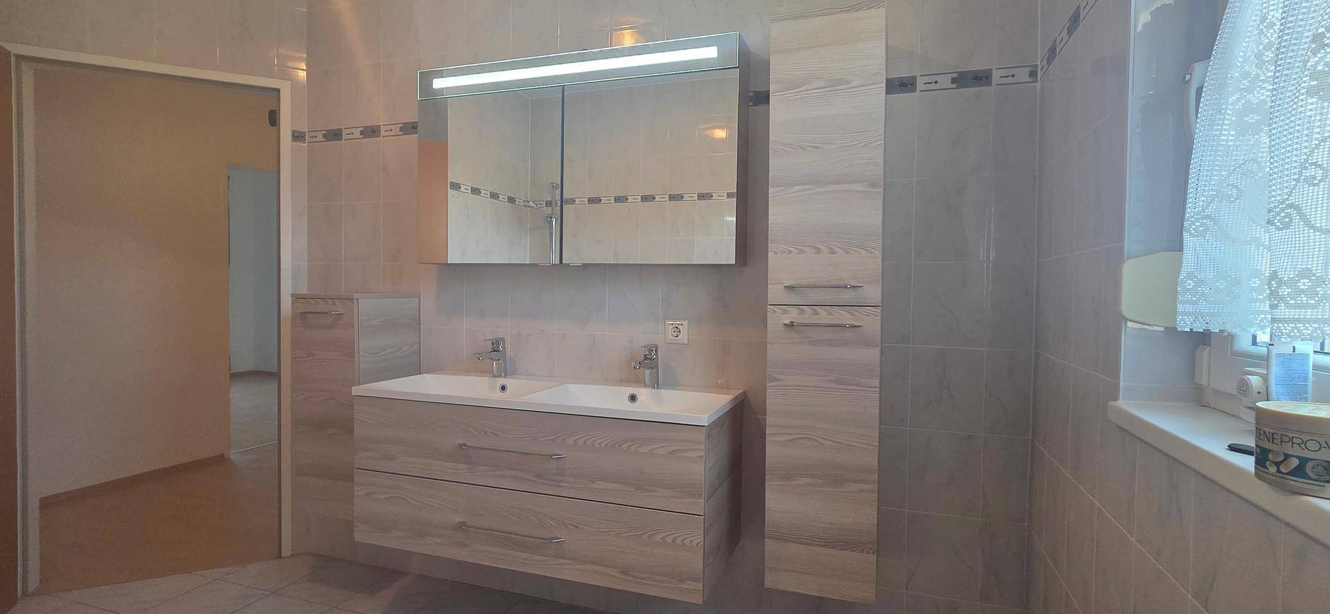 Helles Badezimmer mit Doppelwaschbecken, Spiegelschrank und modernen Holzmöbeln.