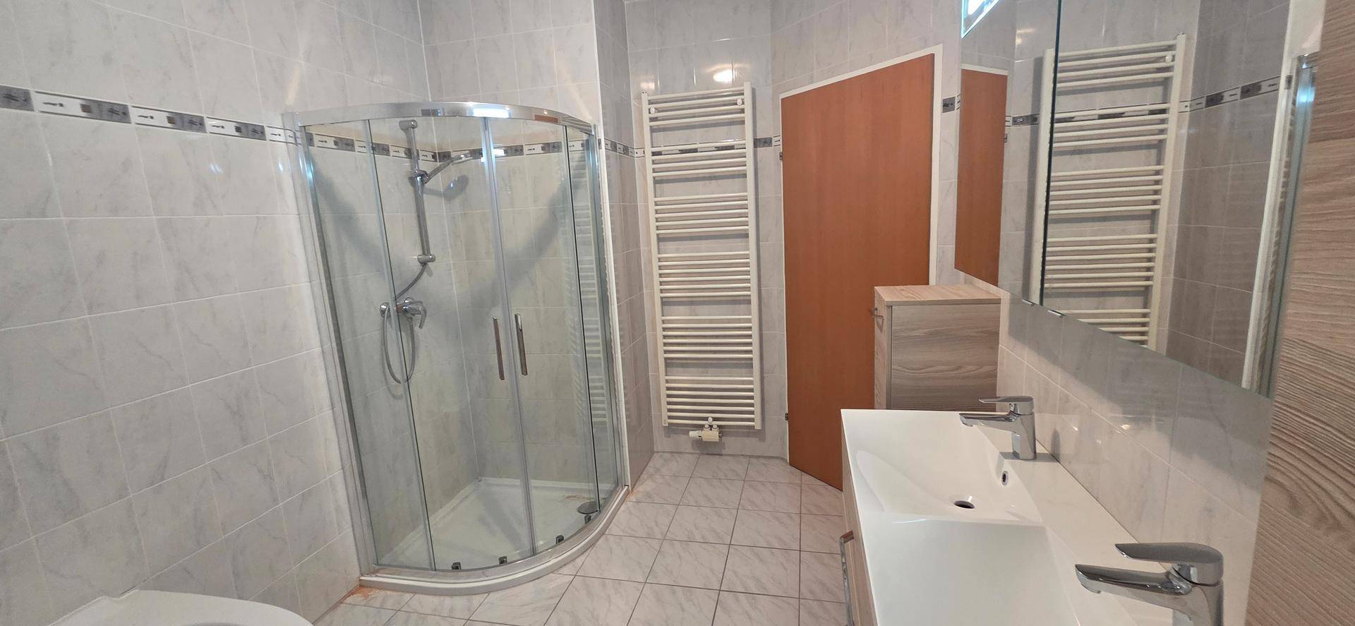 Modernes Badezimmer mit Duschkabine, beheiztem Handtuchhalter und hellem Fliesenboden.