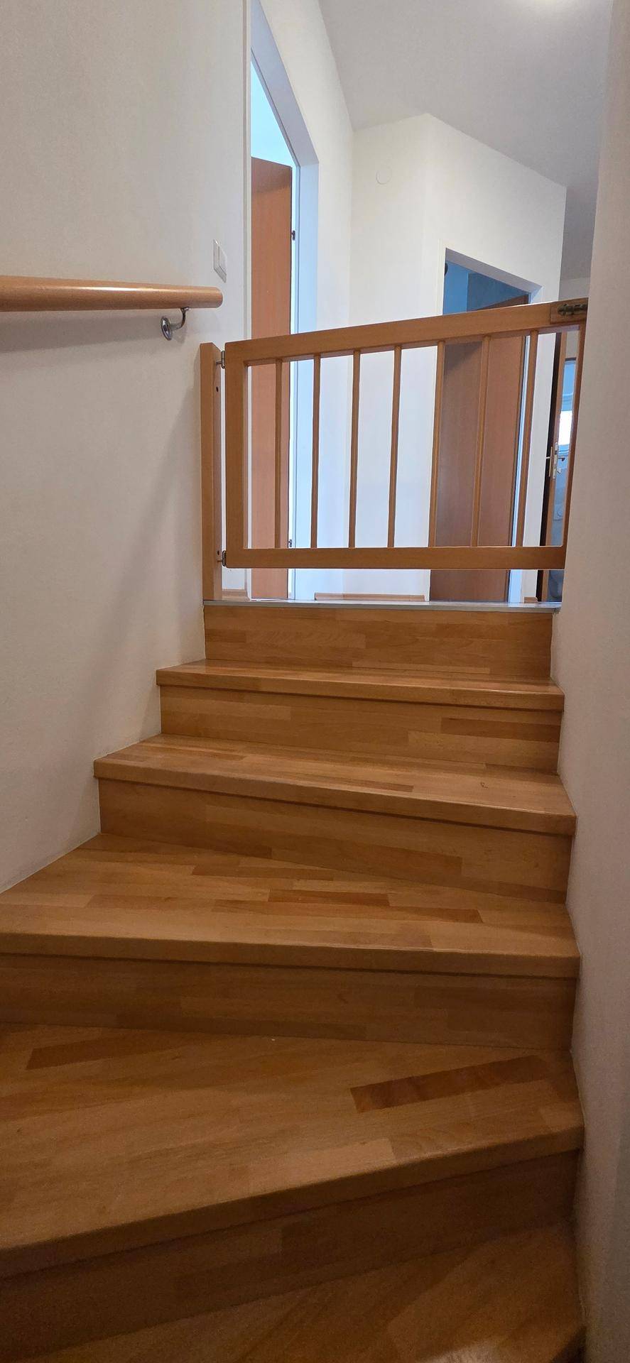 Helle Holztreppe mit Kinderschutzgitter, die zu den oberen Wohnbereichen führt.