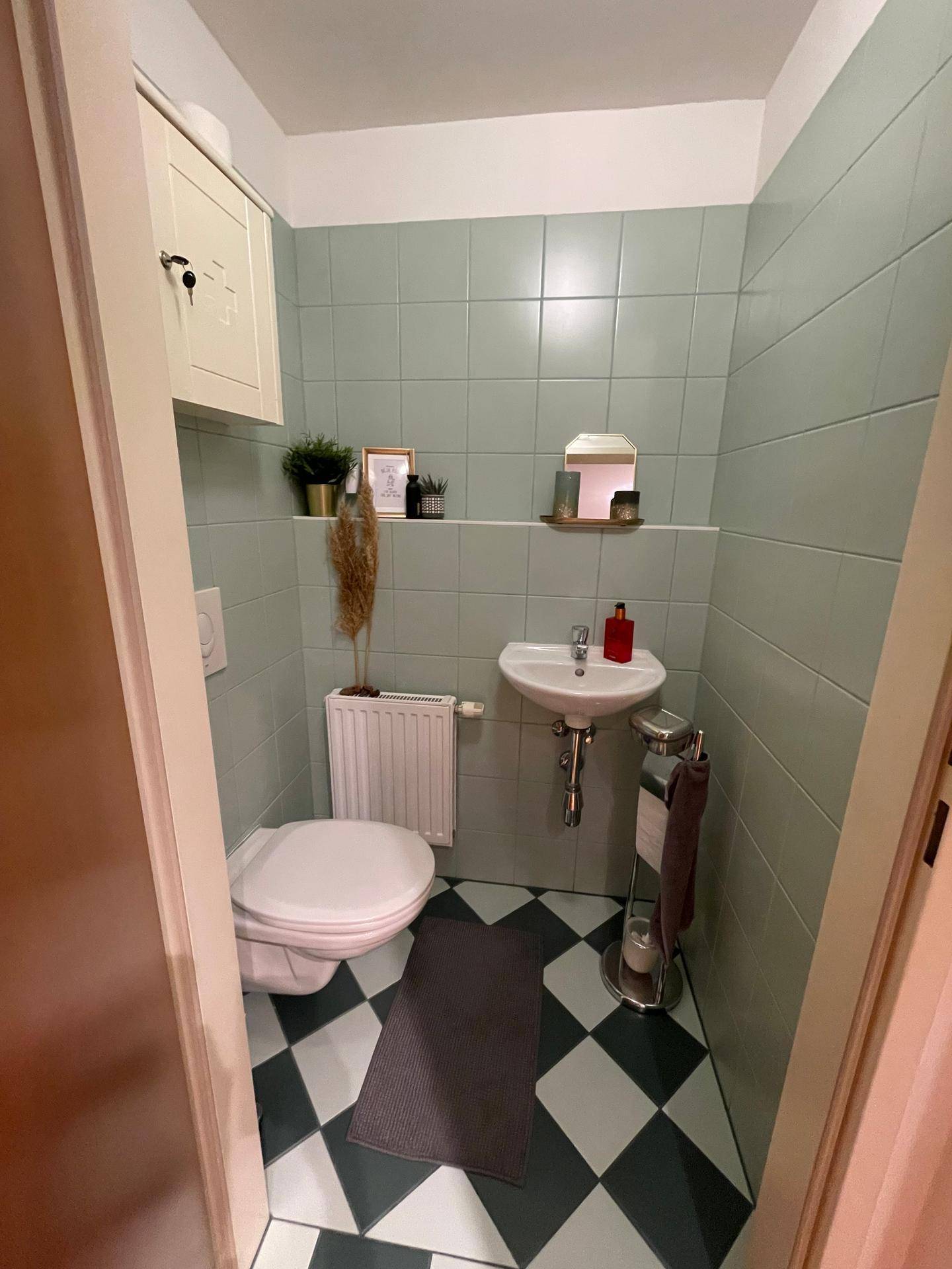 Separates WC mit hellgrünen Fliesen, kariertem Boden und kleinem Waschbecken, praktisch und kompakt.