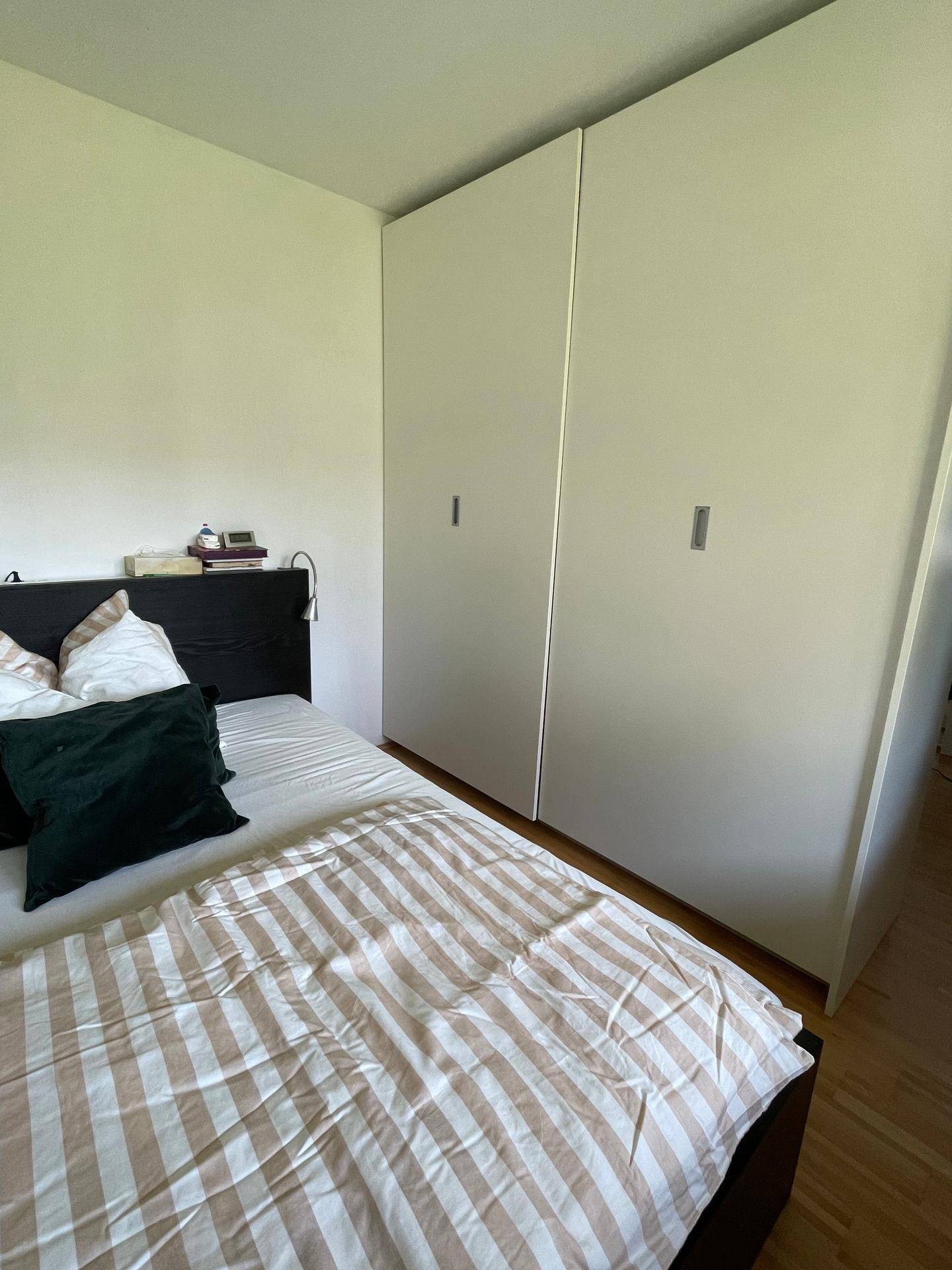 Schlafzimmer mit integrierten weißen Kleiderschränken und dunklem Bett, bietet viel Stauraum und Holzfußboden.