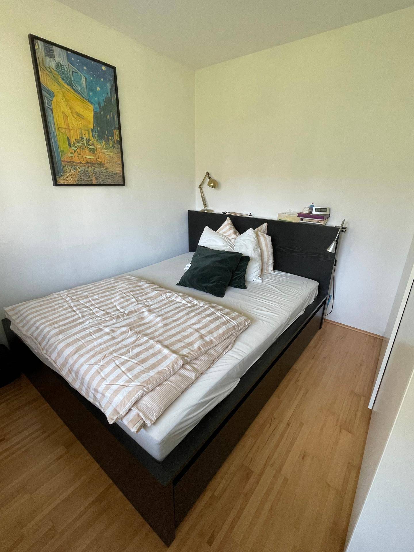 Schlafzimmer mit dunklem Bettrahmen, gestreifter Bettwäsche und Kunstwerk an der Wand, ausgestattet mit Holzfußboden.