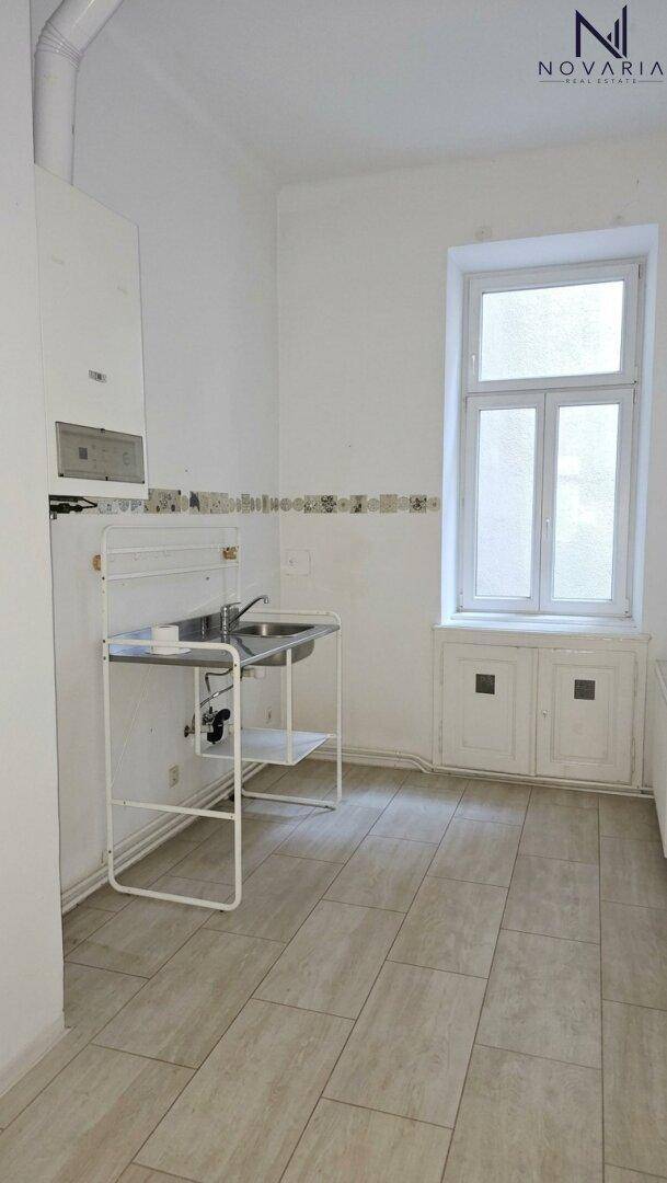 Einfache Küche mit Spülbecken, Boiler und Fliesenboden, bereit für eine individuelle Gestaltung.