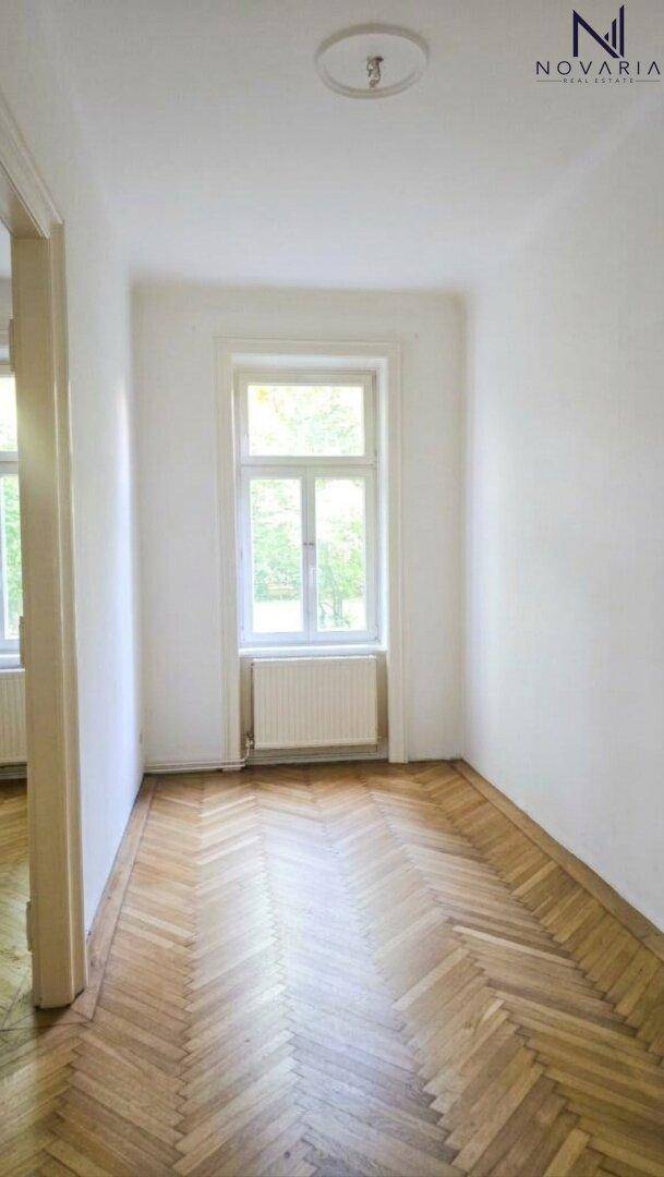 Freundliches Zimmer mit klassischem Fischgrätparkett und einem großen Fenster für natürliche Belichtung.