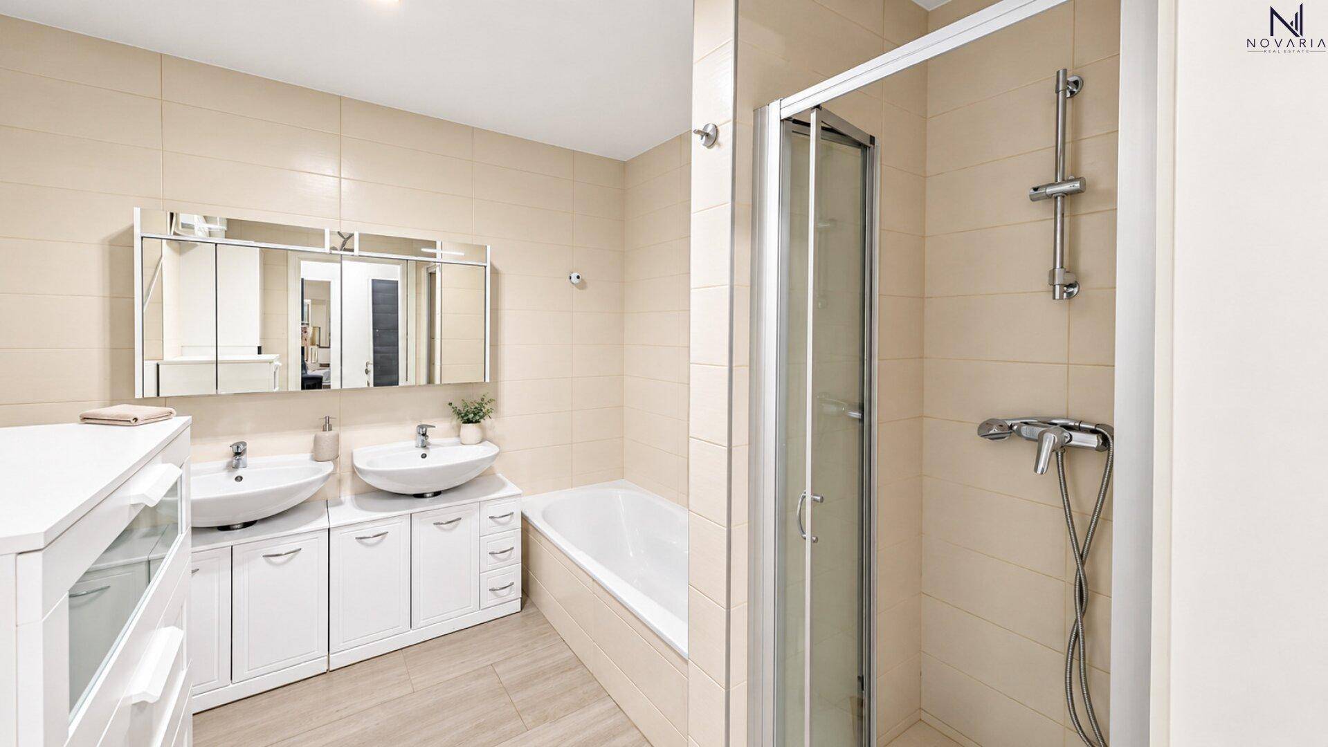 Helles Badezimmer mit Doppelwaschbecken, Badewanne und separater Duschkabine in beigen Fliesen.
