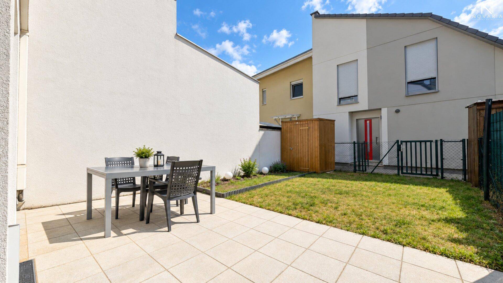 Sonniger Terrassenbereich mit Sitzgelegenheiten und kleinem Rasenstück hinter dem Gebäude.