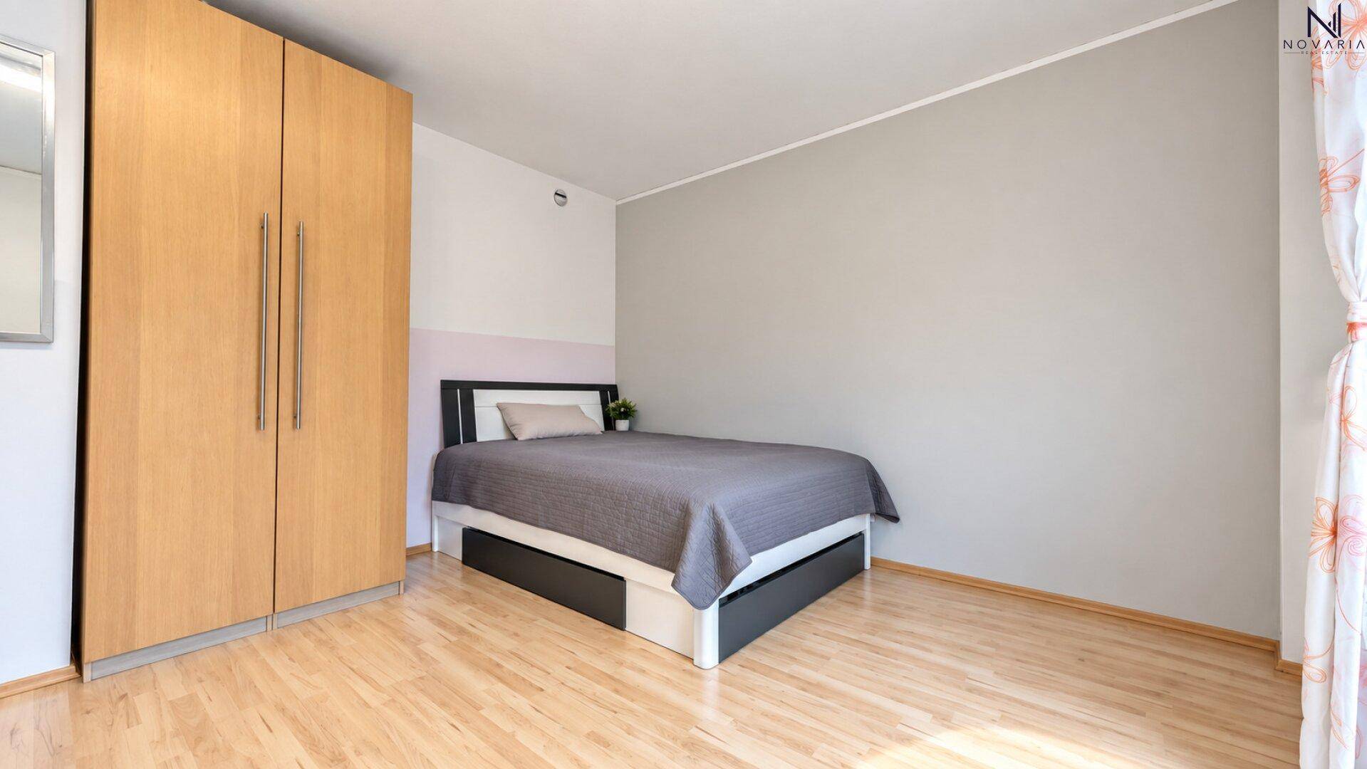 Schlichtes Schlafzimmer mit Doppelbett, Holzschrank und hellem Laminatboden.