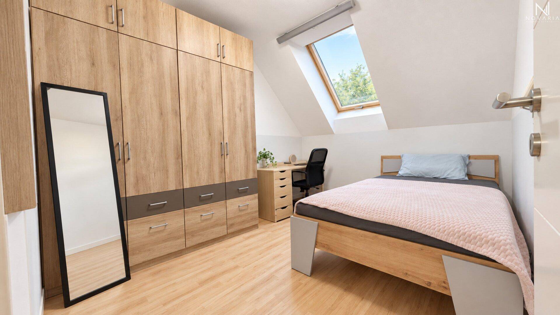 Helles Schlafzimmer im Dachgeschoss mit großem Kleiderschrank, Bett und Schreibtisch.