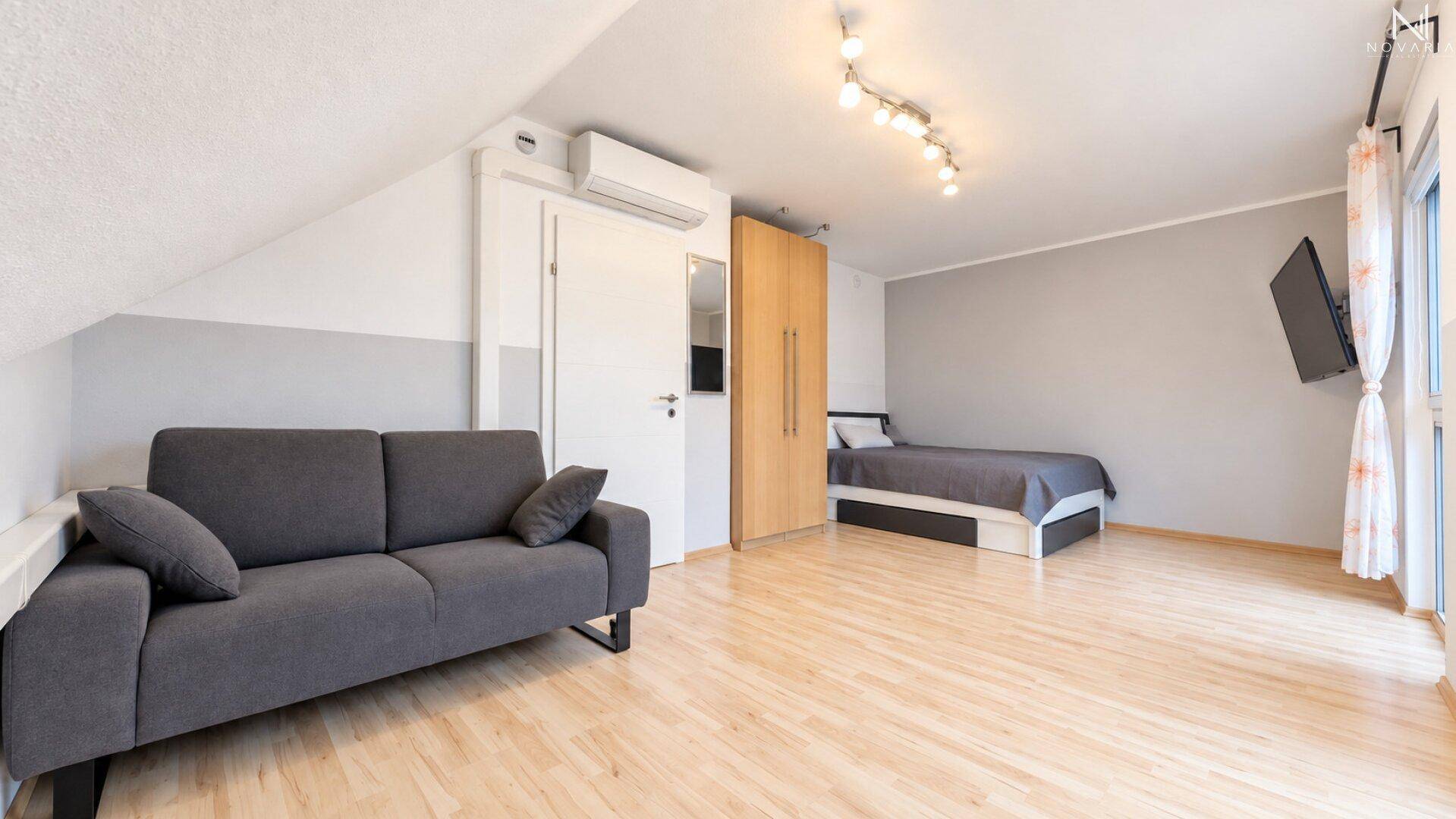 Dachgeschosszimmer mit Schlafbereich, Sofa und Klimaanlage unter der Dachschräge.