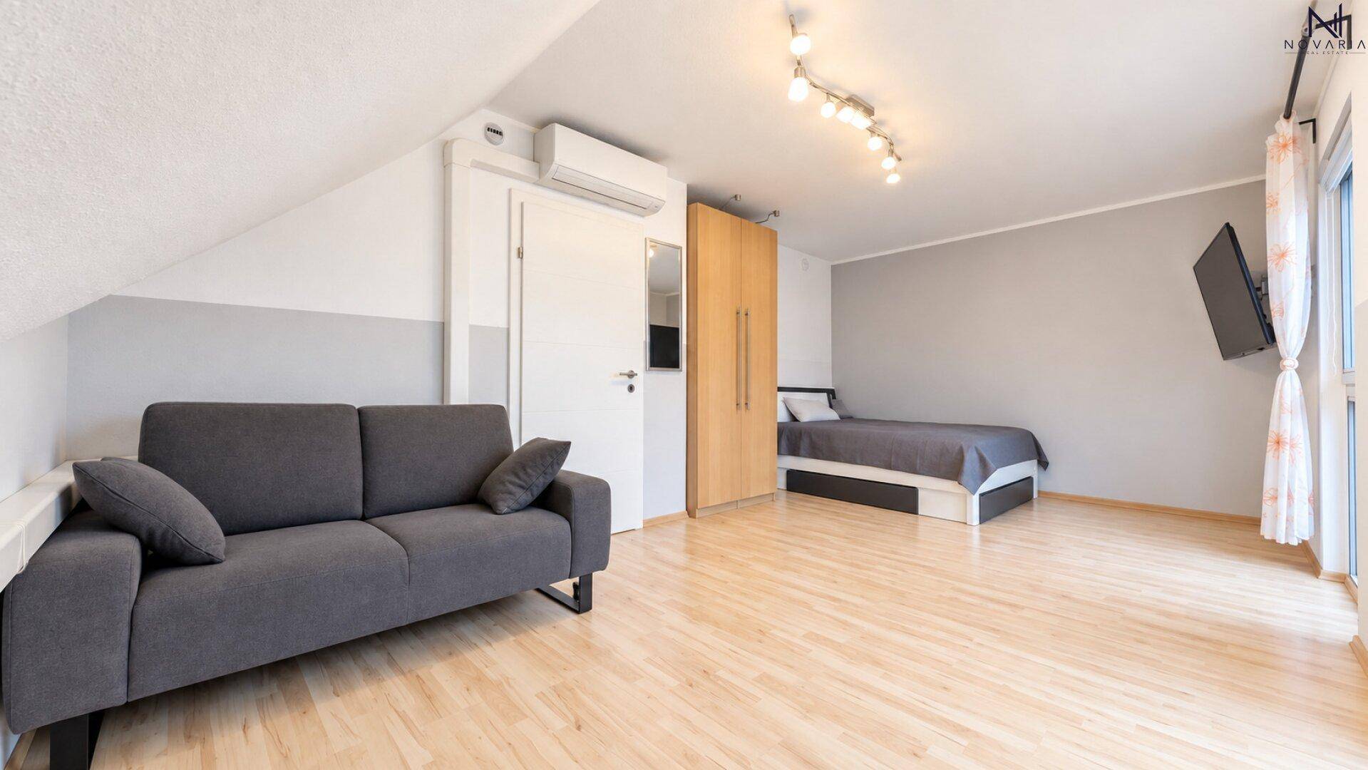 Gemütliches Dachzimmer mit Sofa, Einzelbett und schrägen Wänden, ausgestattet mit Klimaanlage.
