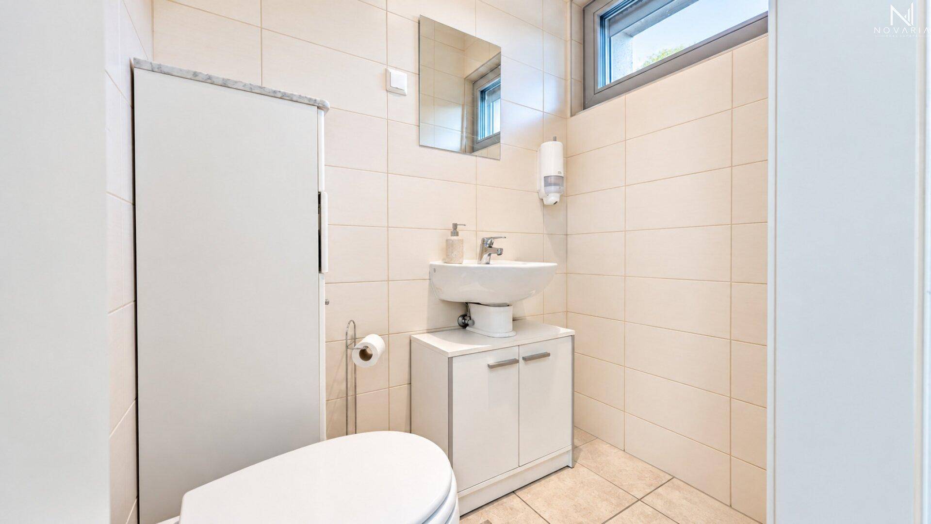 Kleines Gäste-WC mit Fenster, Waschbecken und wandmontierter Toilette.