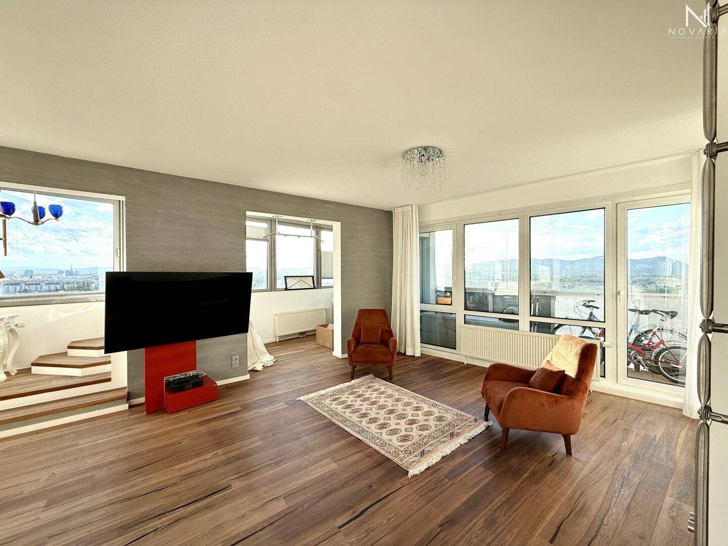 Gemütliches Wohnzimmer mit Holzboden, bequemen Sesseln und großen Fenstern mit Weitblick.