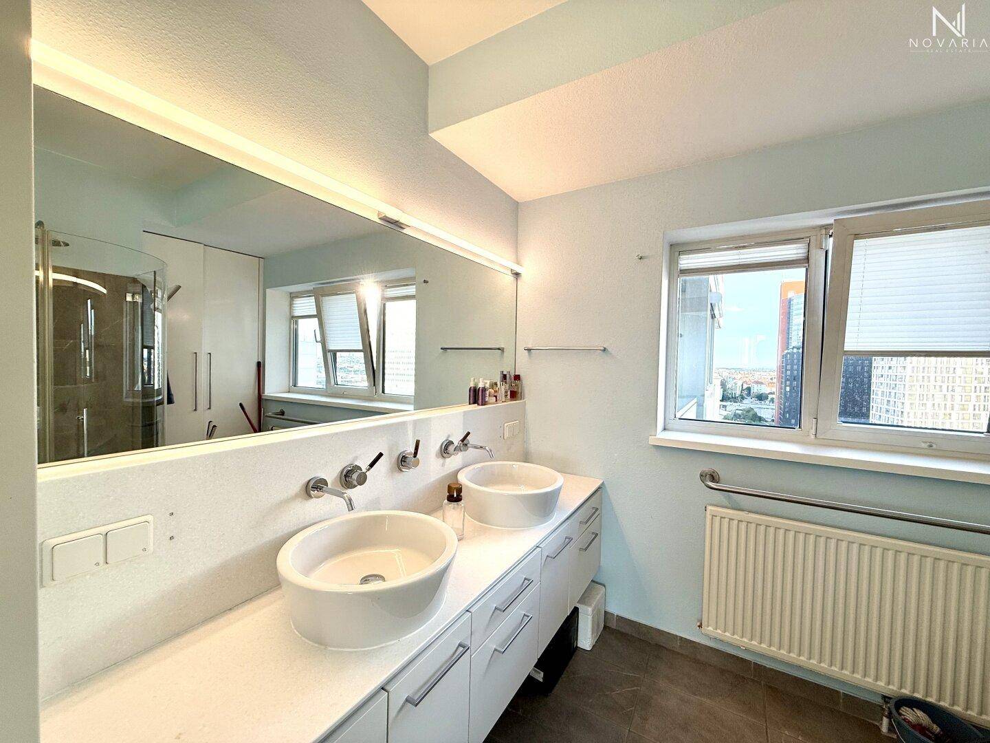 Modernes Badezimmer mit Doppelwaschbecken, großem Spiegel und Fenster mit Stadtblick.