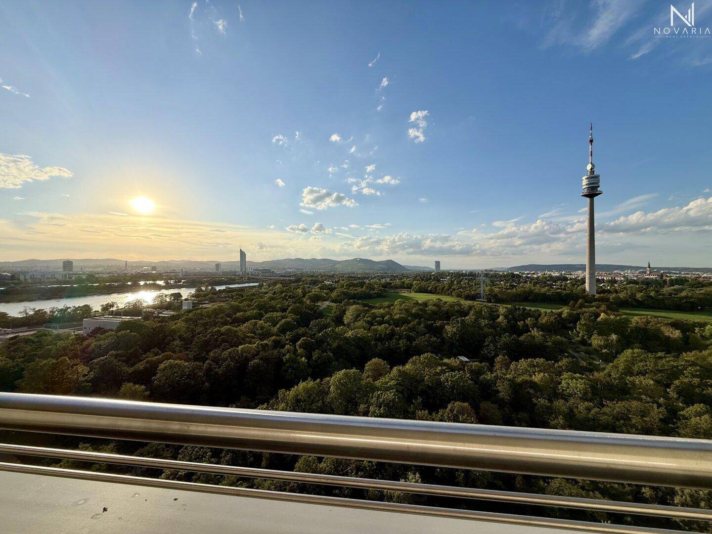 Atemberaubender Panoramablick vom Balkon über die Stadt, grüne Parks und den Donauturm bei Sonnenuntergang.