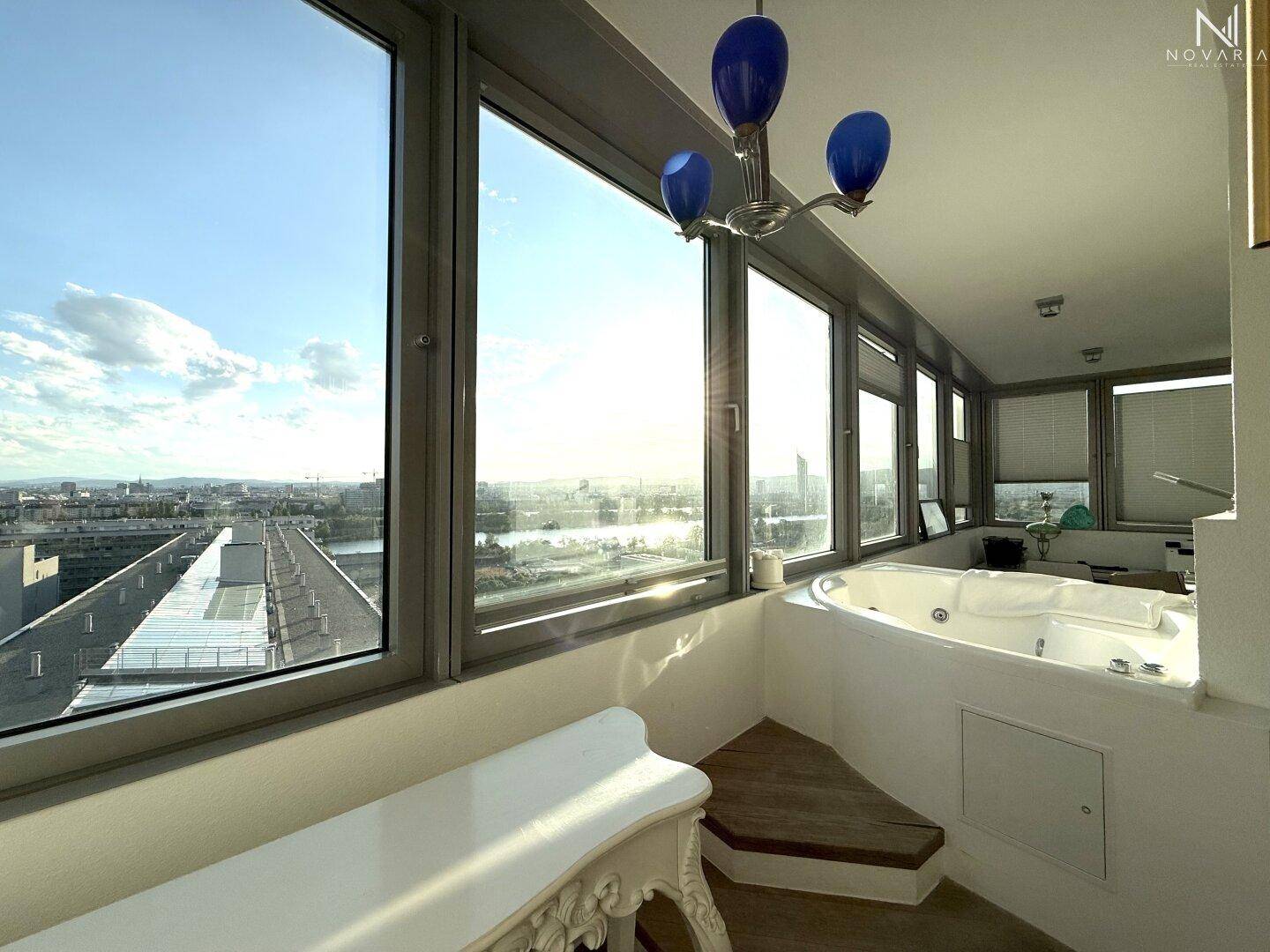 Heller Raum mit Whirlpool und großen Fenstern, die einen weiten Blick über die Stadt bieten.