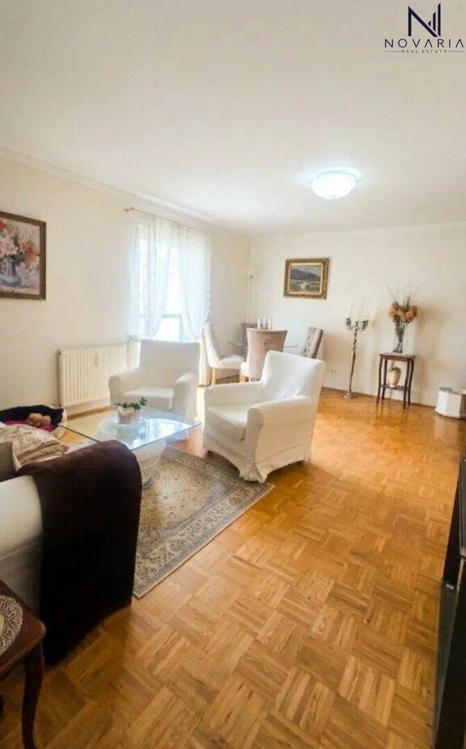 Geräumiges Wohnzimmer mit Parkettboden, weißen Sesseln und einem Esstisch im Hintergrund.