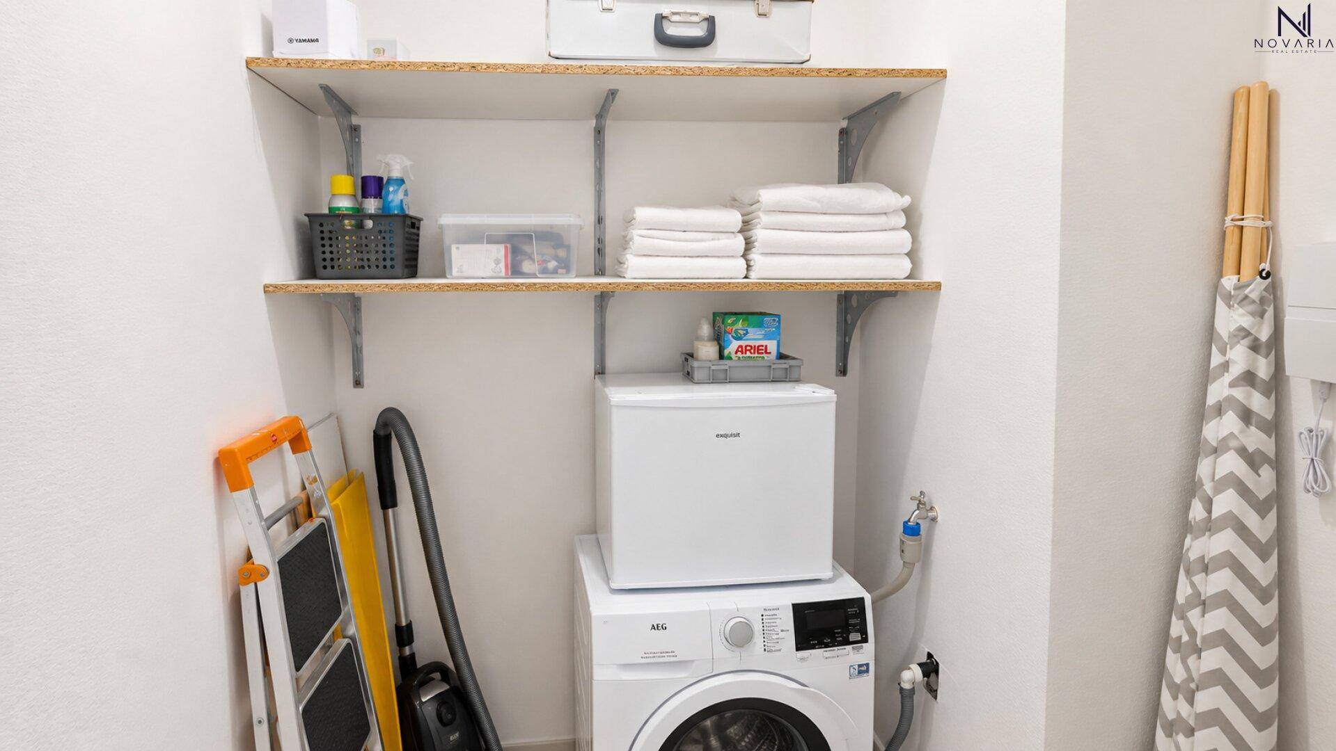 Praktischer Hauswirtschaftsraum mit Waschmaschine, kleinem Kühlschrank und Regalen für Stauraum.