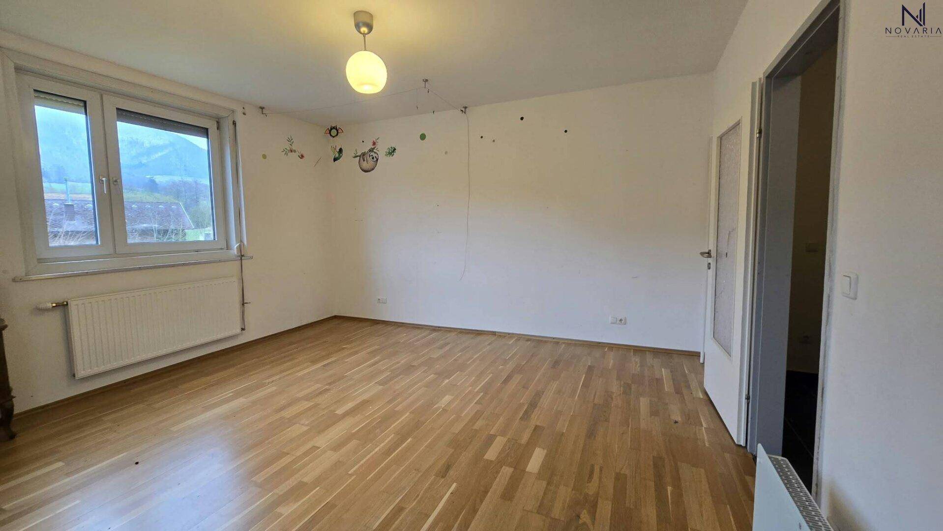 Leeres Zimmer mit hellem Holzboden, großem Fenster und Heizkörper, bereit zur individuellen Einrichtung.