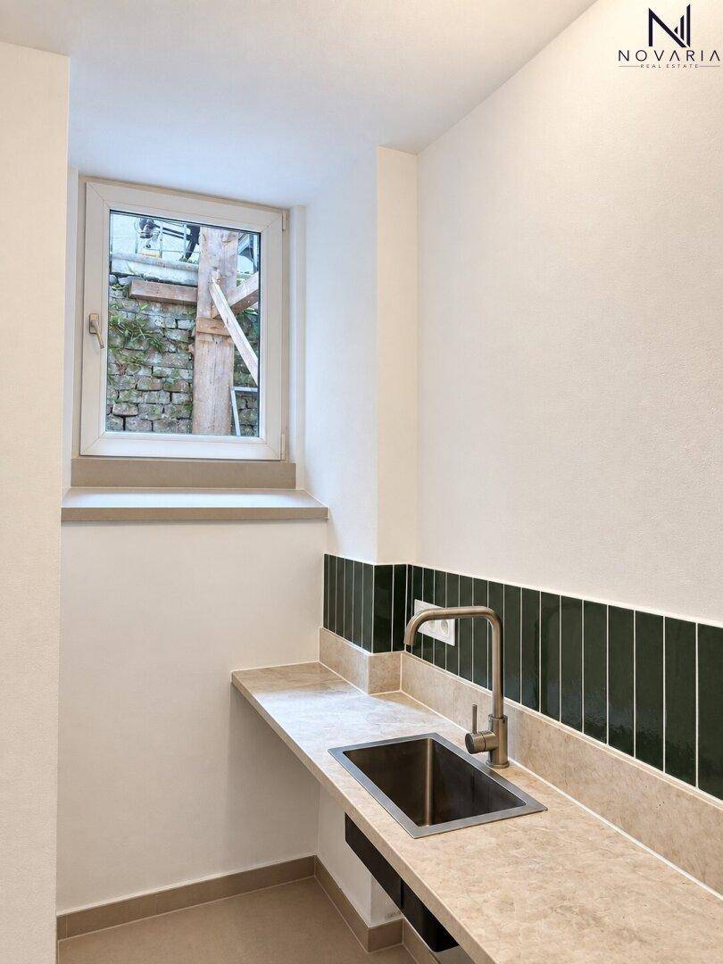 Kleiner Hauswirtschaftsraum mit Waschbecken, Arbeitsplatte, dunklen Fliesen und Fenster.