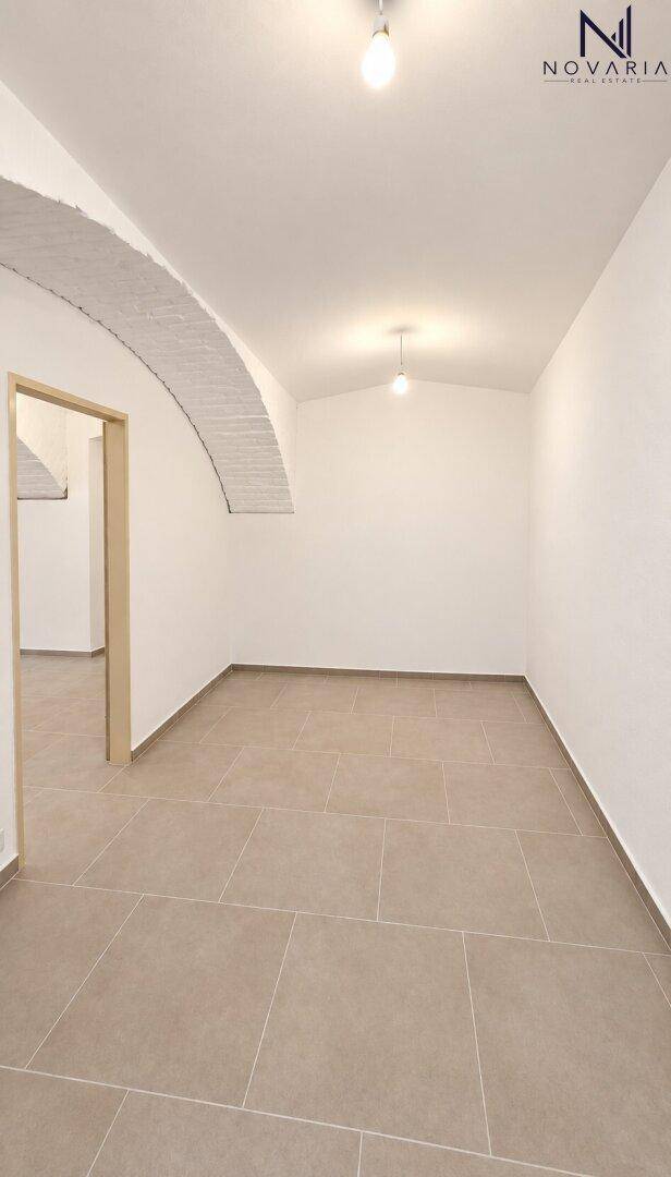 Renovierter Kellerraum mit Gewölbedecke, hellem Fliesenboden und schlichten Wänden.
