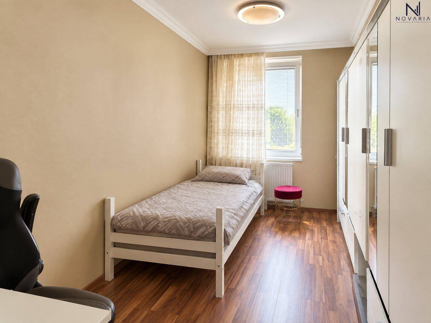 Helles Schlafzimmer mit Einzelbett, Schrank und Fenster.