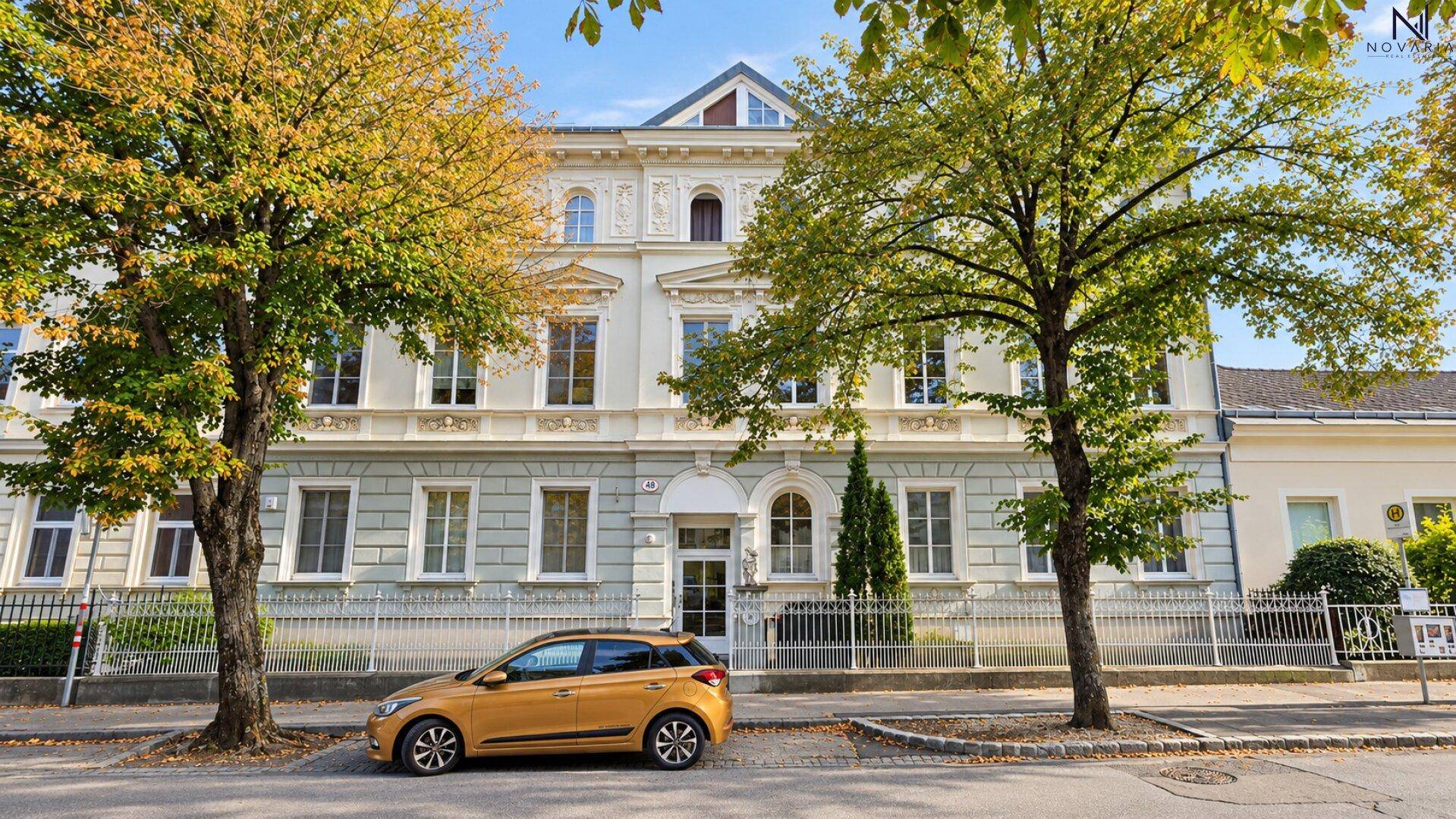 Ansicht des Gebäudes von der Straße mit Bäumen und klassischer Architektur.