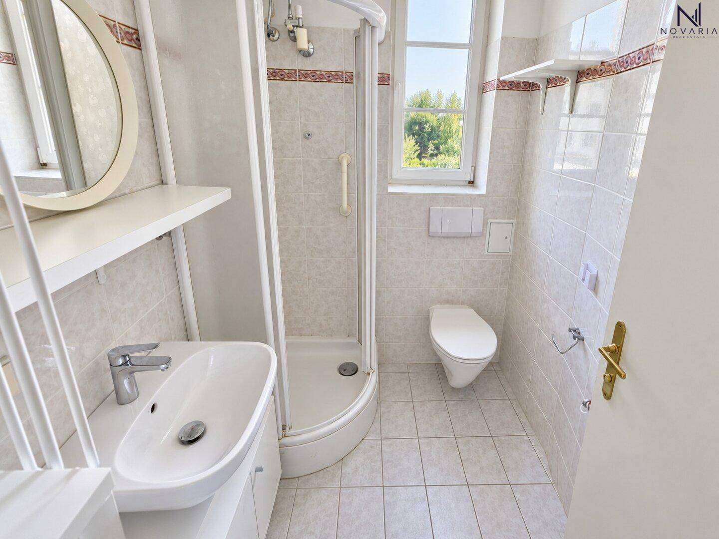 Helles Badezimmer mit Dusche, WC, Waschbecken und Fenster, ausgestattet mit Haltegriffen.