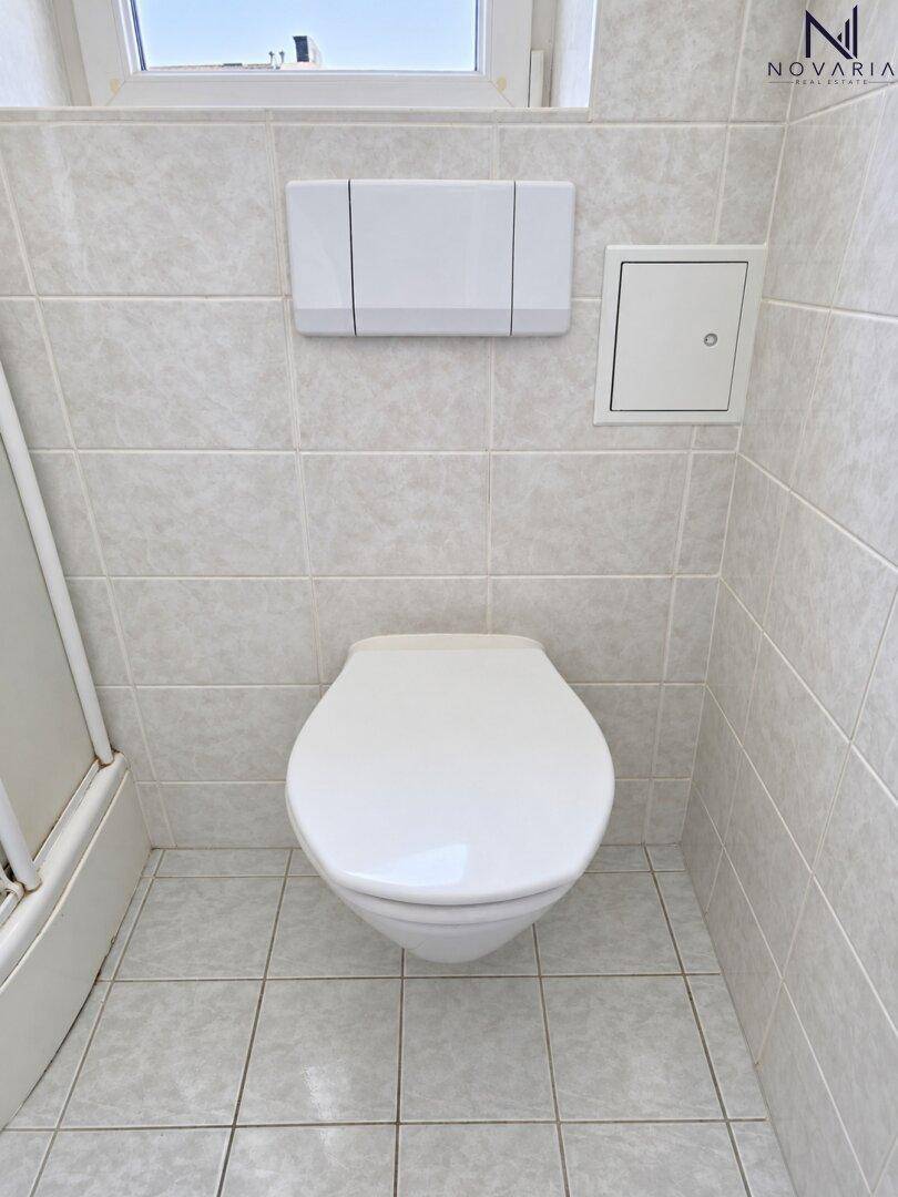 Modernes Wand-WC in einem gefliesten Badezimmer mit sauberer und funktionaler Ausstattung.