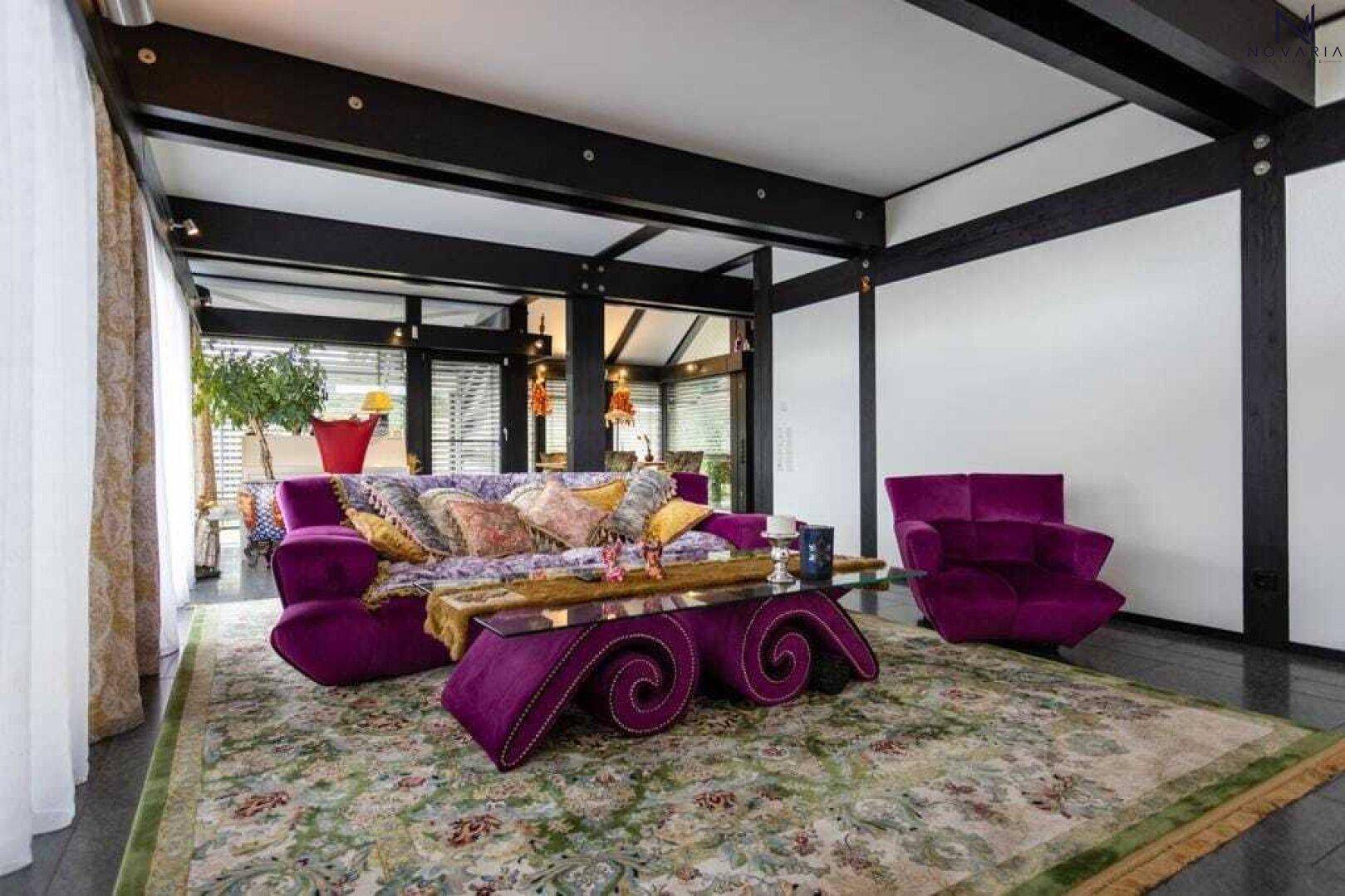 Farbenfrohes Wohnzimmer mit auffälligen violetten Möbeln, gemustertem Teppich und dunklen Holzbalken.