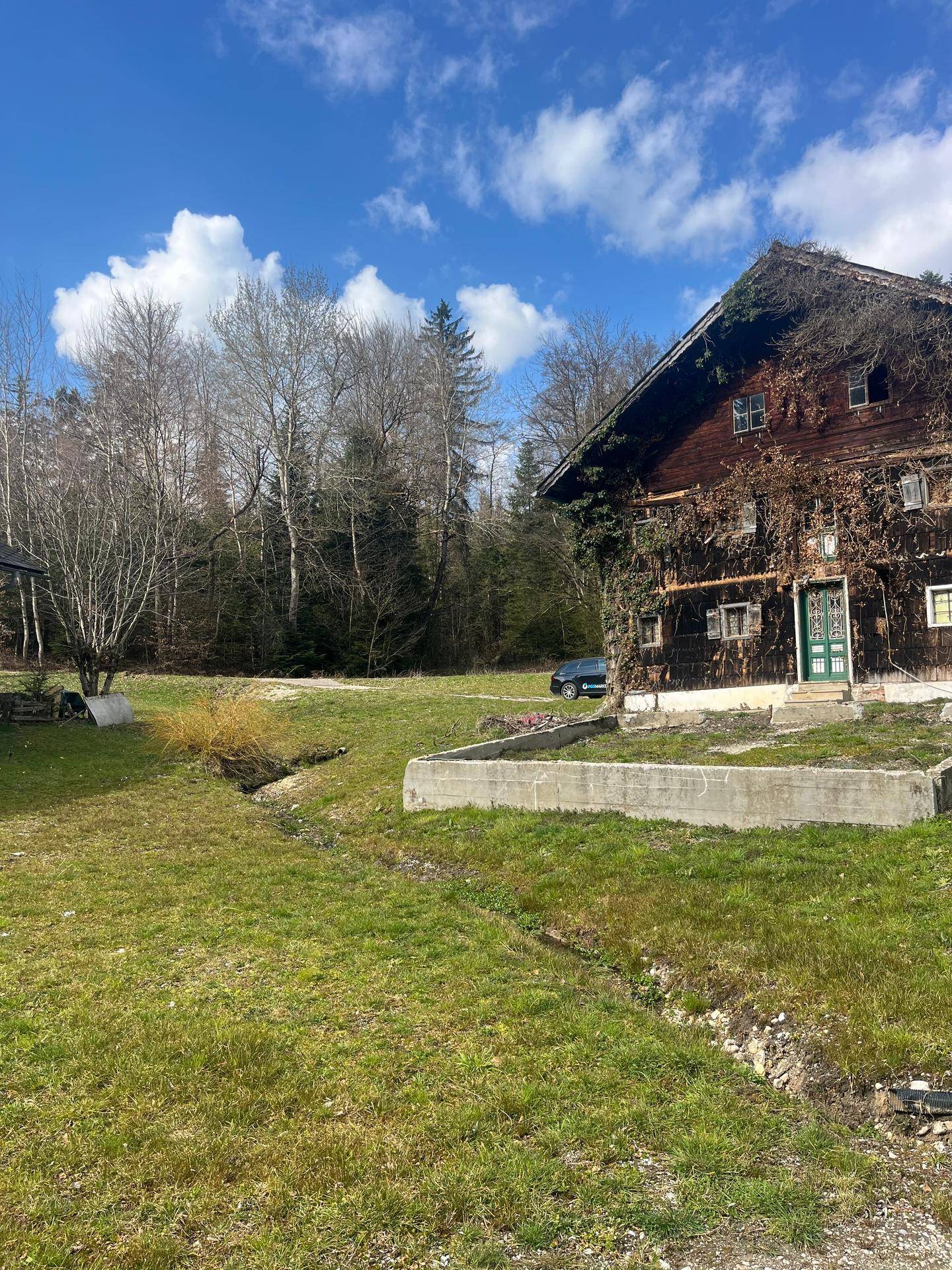 Rustikales Holzhaus umgeben von einer weitläufigen Wiese und dichtem Wald im Hintergrund.