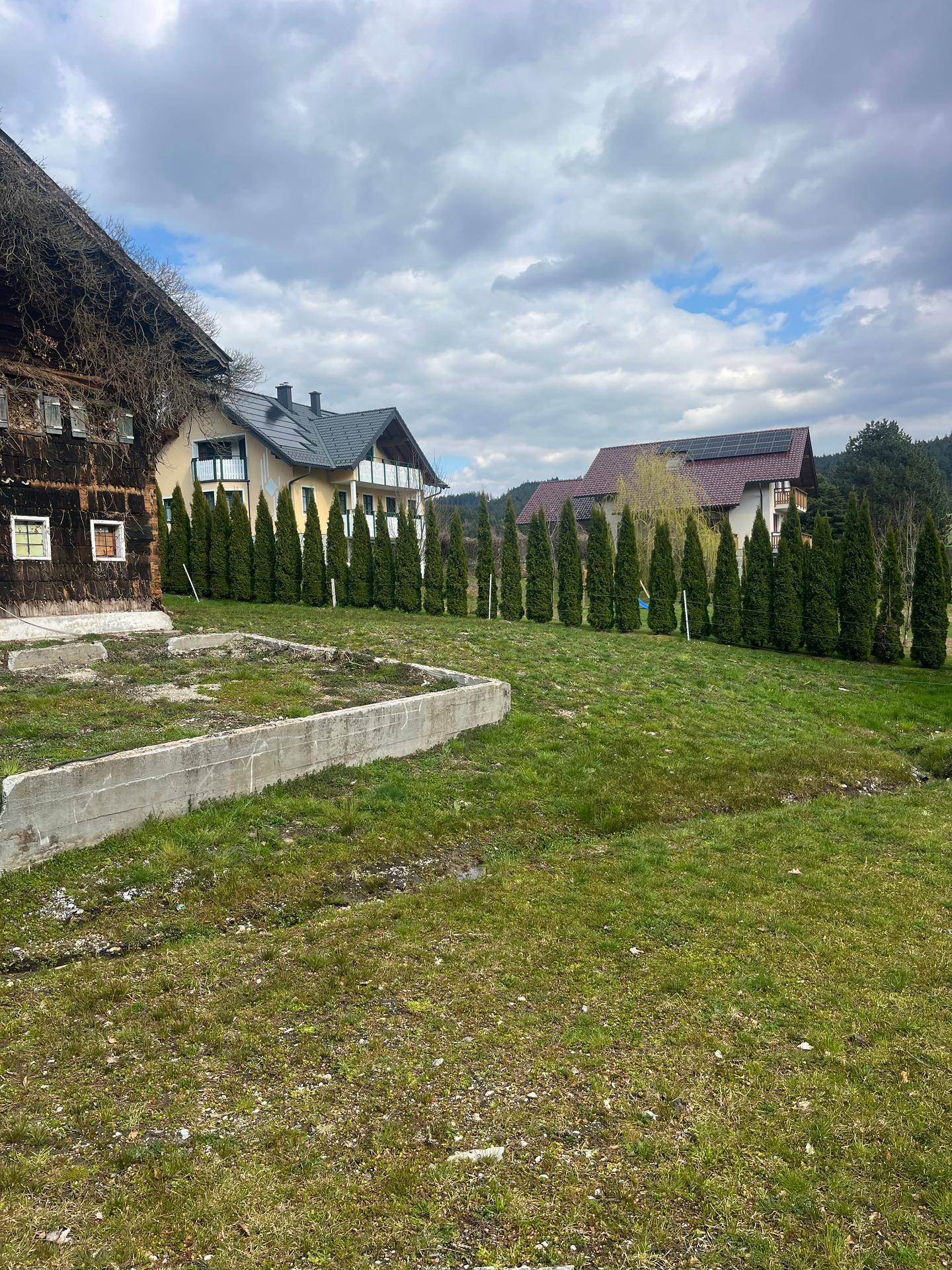 Weitläufige Wiese neben dem Holzhaus mit Blick auf ein Nachbargebäude mit Solaranlage.