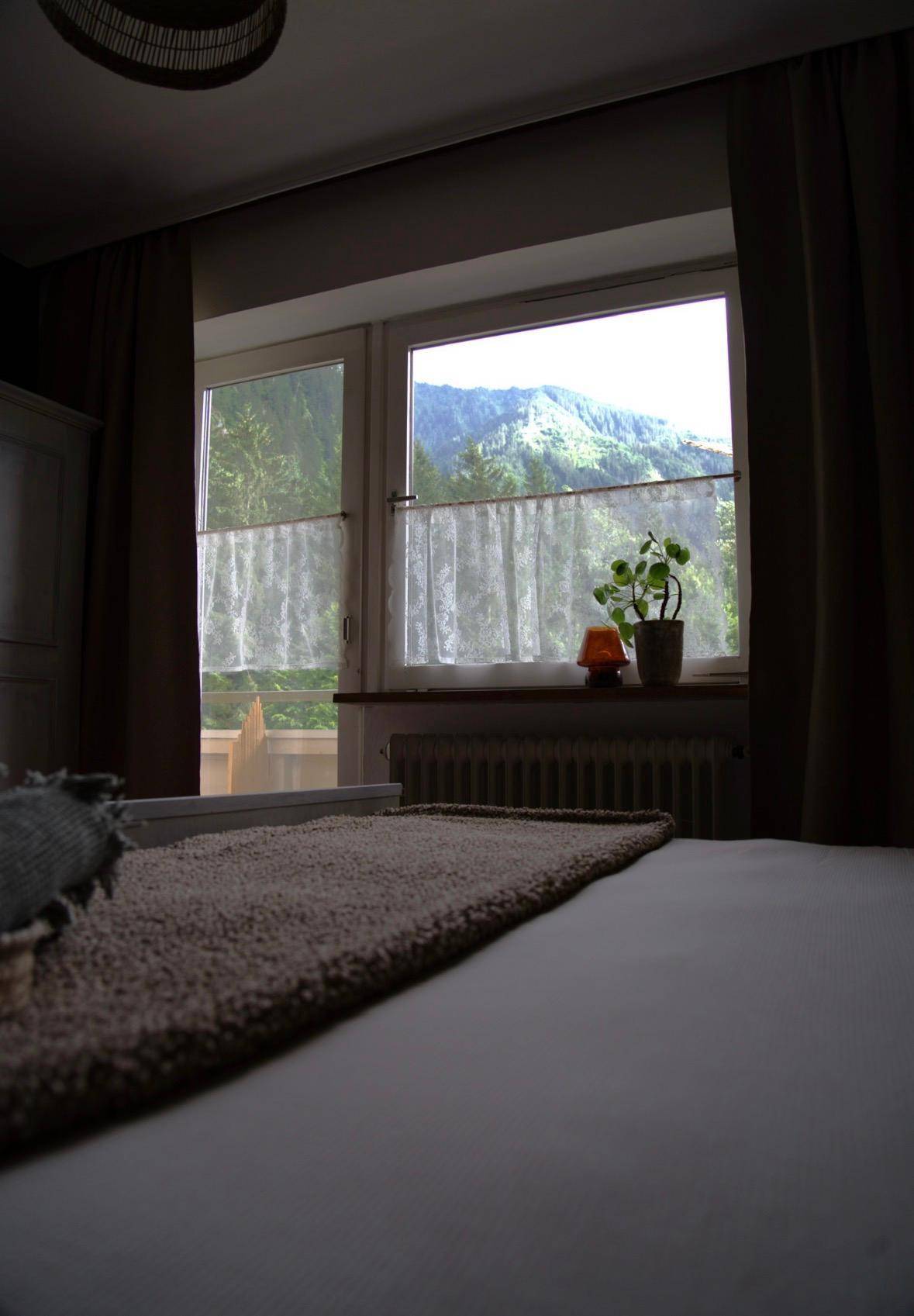 Schlafzimmer mit Bergblick, großem Fenster und einfacher, funktionaler Einrichtung.