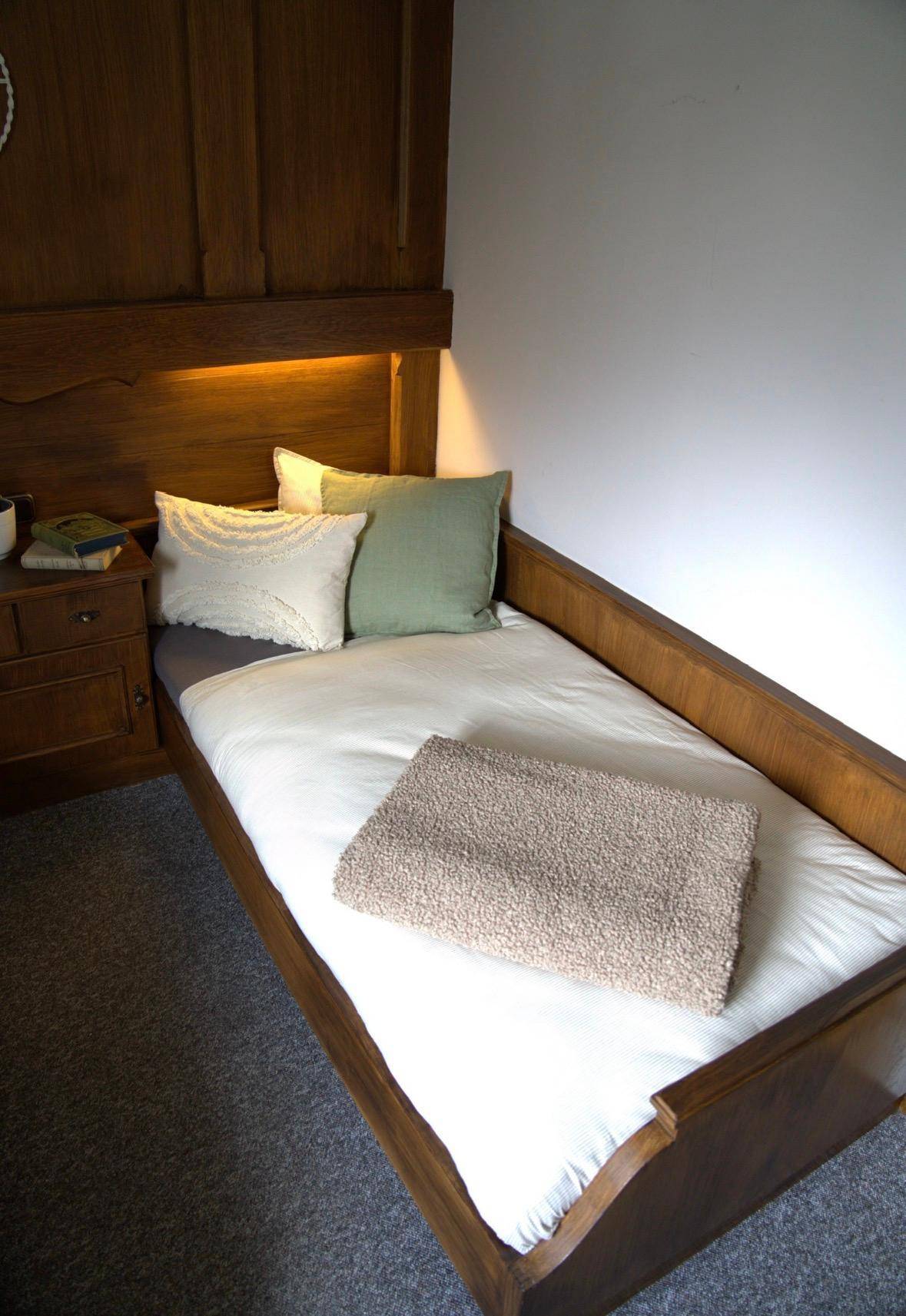Einzelbett in einem Schlafzimmer mit Holzmöbeln und schlichter, sauberer Ausstattung.