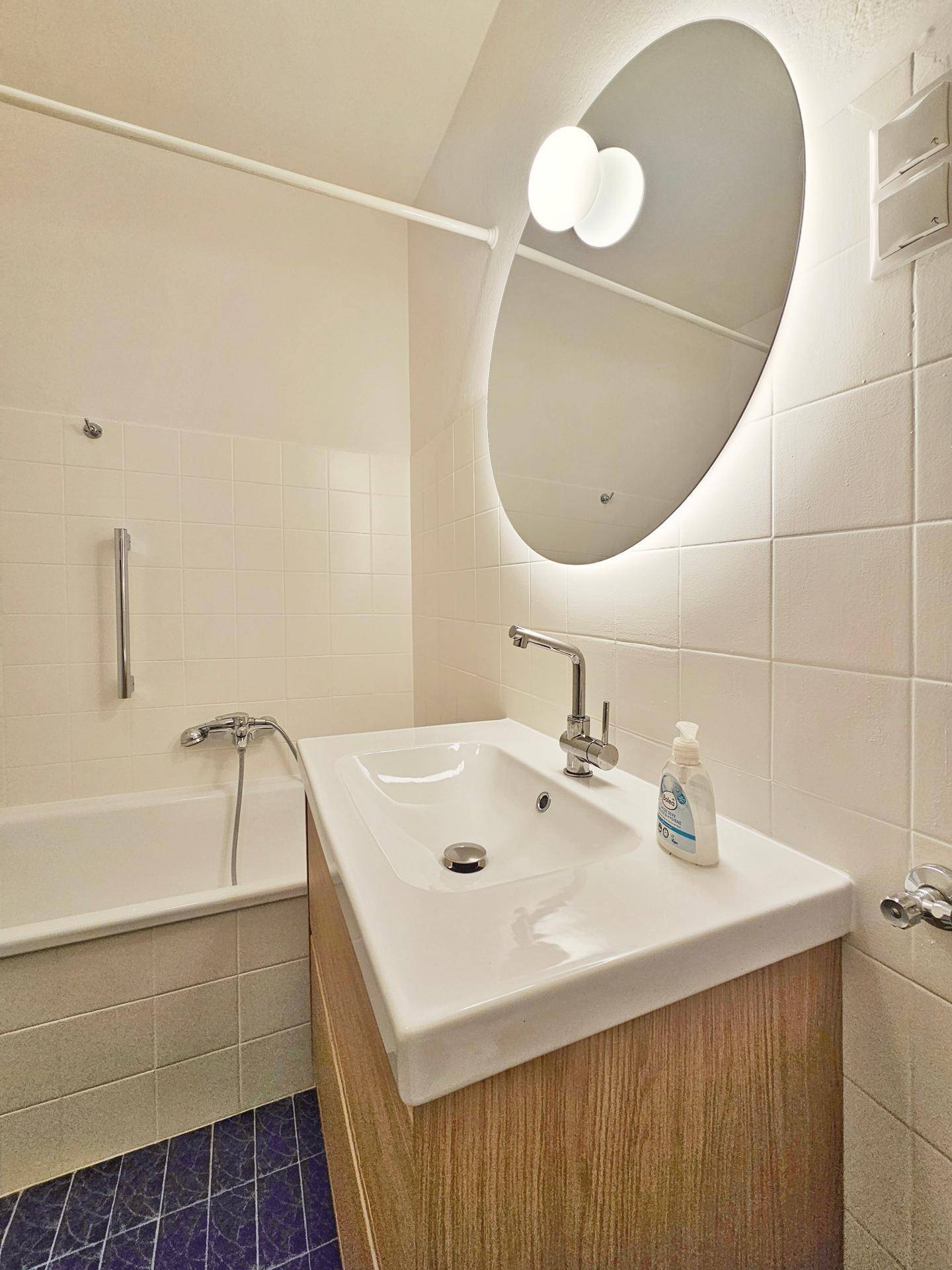 Modernes Badezimmer mit Badewanne, beleuchtetem Spiegel und Holzwaschtischunterschrank.