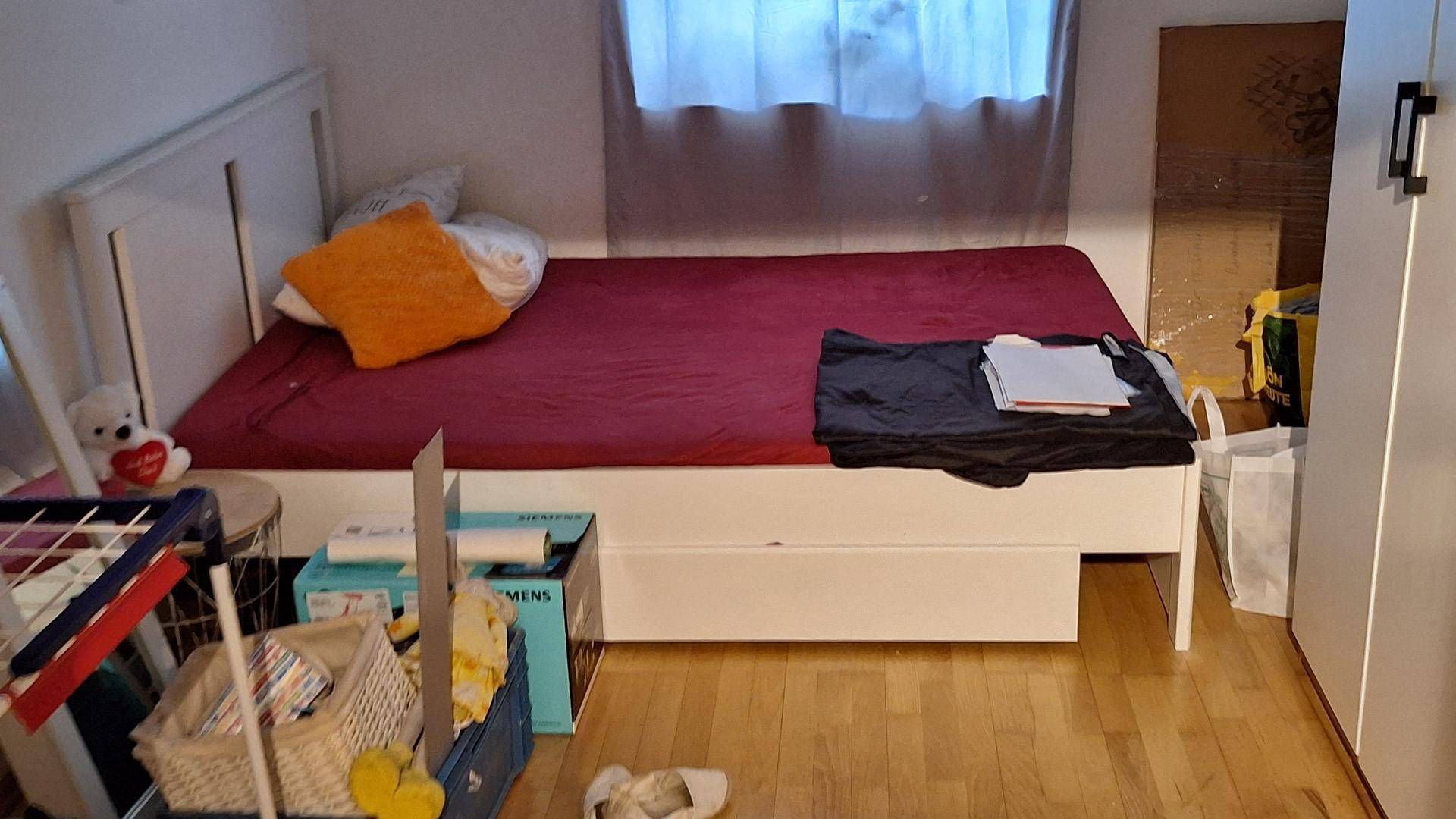 Schlafzimmer mit Einzelbett, Holzboden und Fenster mit Vorhängen.