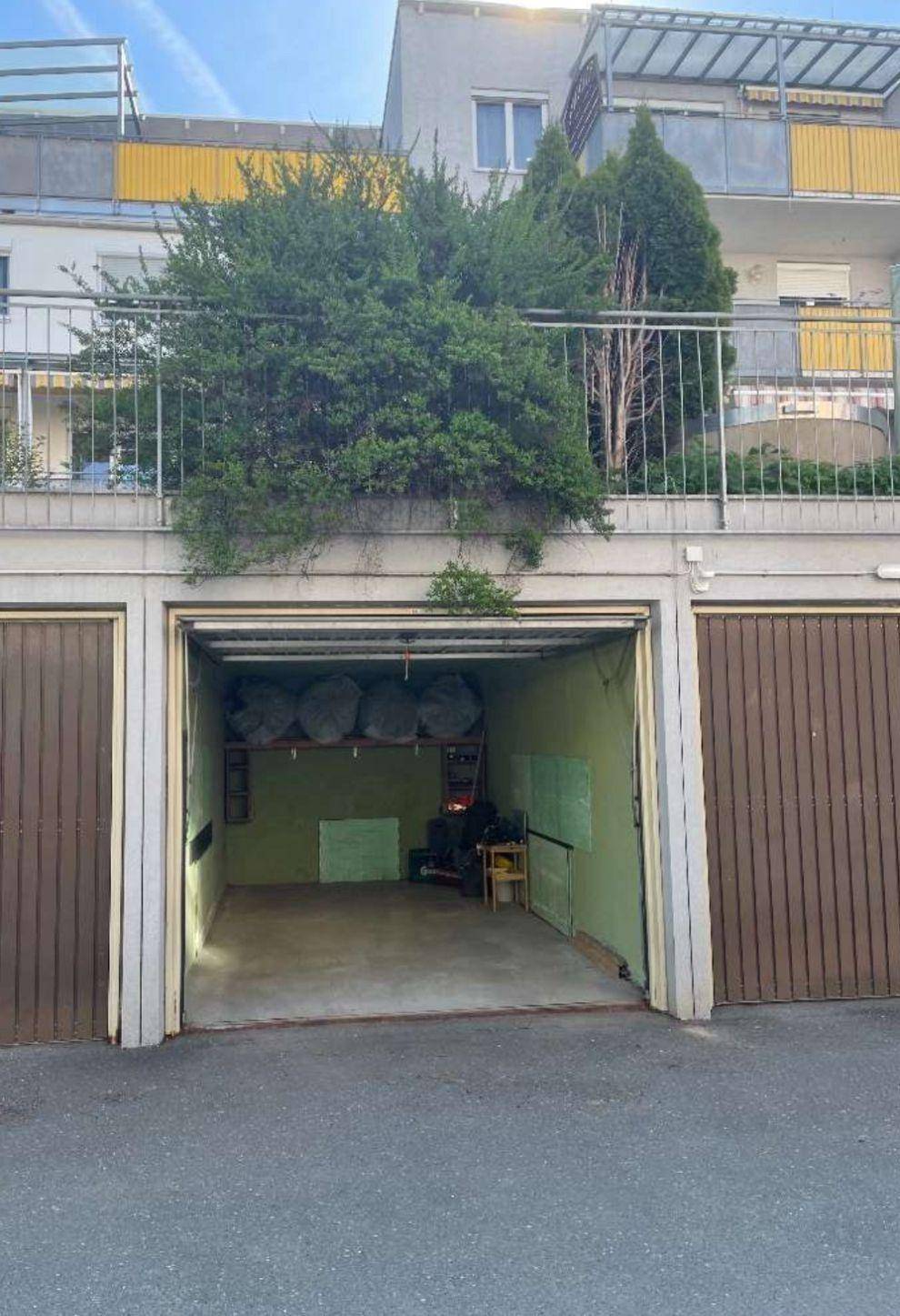Offene Garage mit grün gestrichenen Wänden und braunen Toren unter einem Wohngebäude.