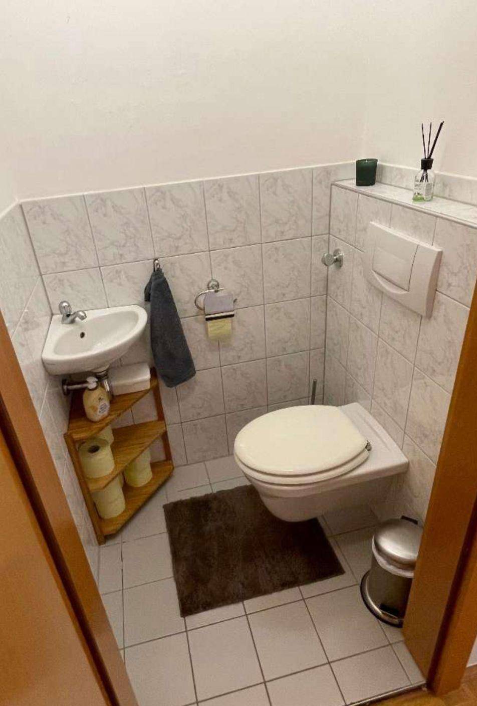 Kleines Gäste-WC mit wandhängender Toilette, Eckwaschbecken und weißen Fliesen.