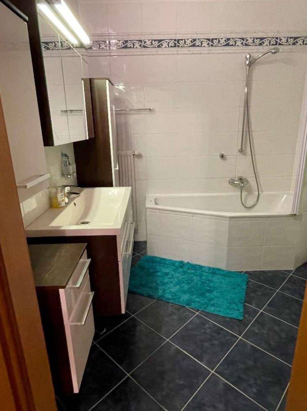 Badezimmer mit Waschtisch, Spiegelschrank und Eckbadewanne mit Duschfunktion.