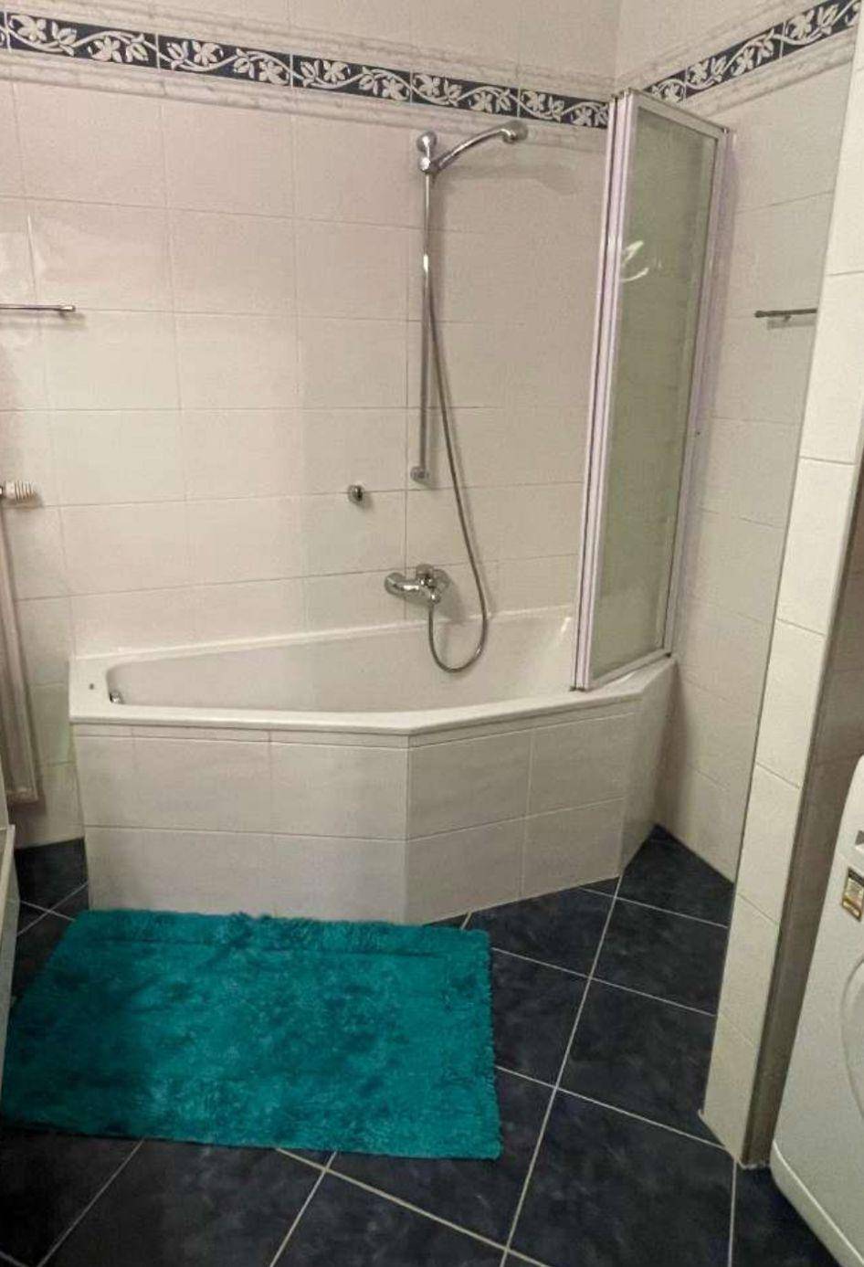 Badezimmer mit Eckbadewanne und Duschabtrennung, ausgestattet mit dunklen Bodenfliesen.