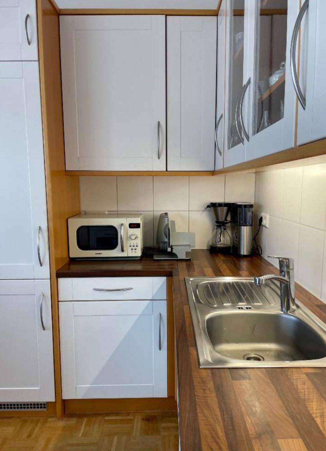 Funktionale Küche mit Spüle, Mikrowelle und Kaffeemaschine, ausgestattet mit Holzarbeitsplatten.