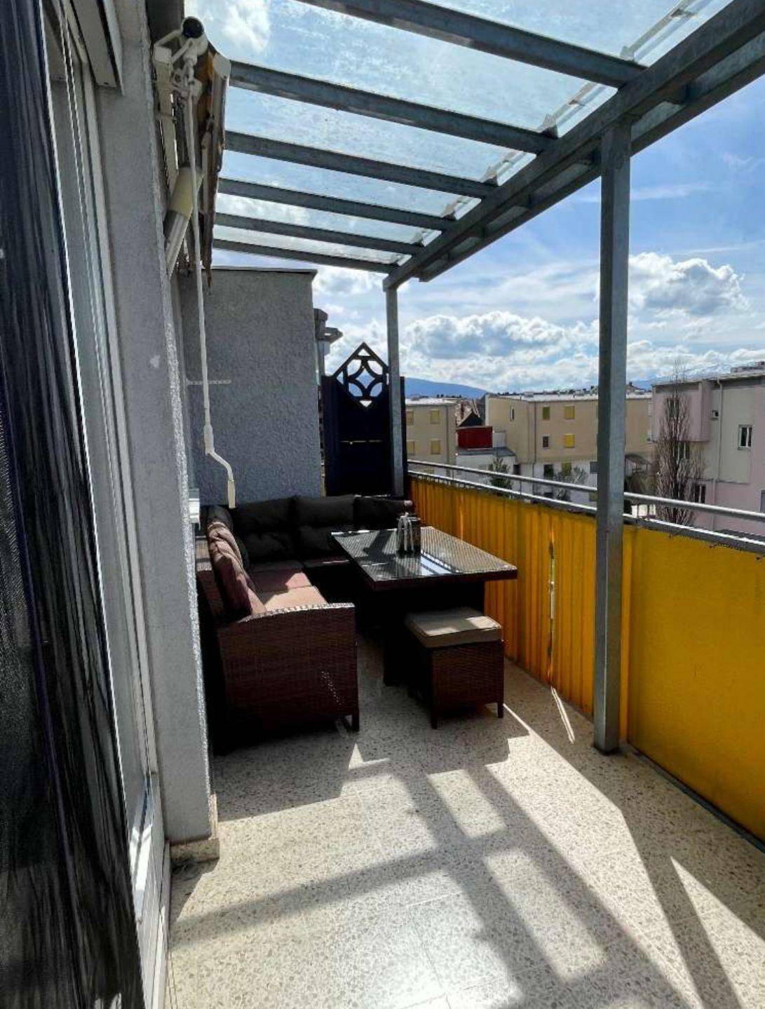 Überdachter Balkon mit bequemen Outdoor-Möbeln und Blick auf die umliegenden Gebäude.