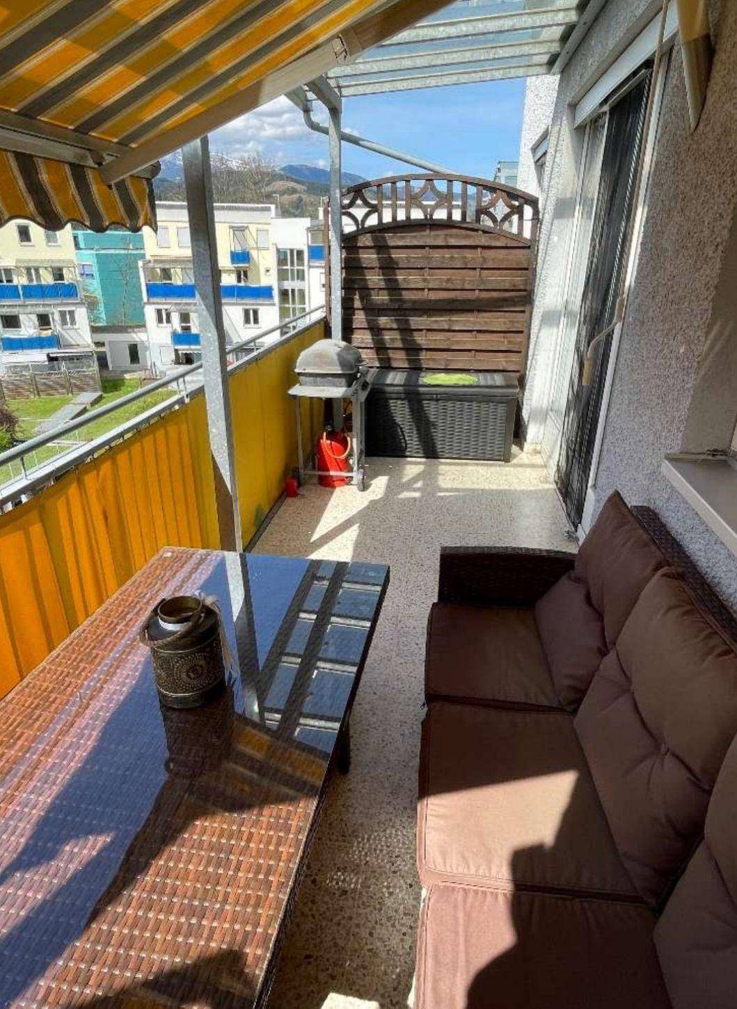 Sonniger Balkon mit Grillbereich, Markise und Blick auf die umliegende Bebauung und Berge.