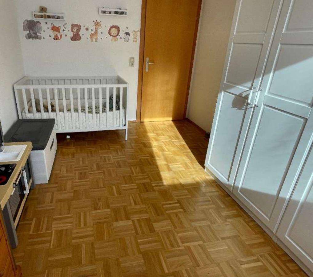 Kinderzimmer mit Babybett, weißem Kleiderschrank und Parkettboden, liebevoll dekoriert.